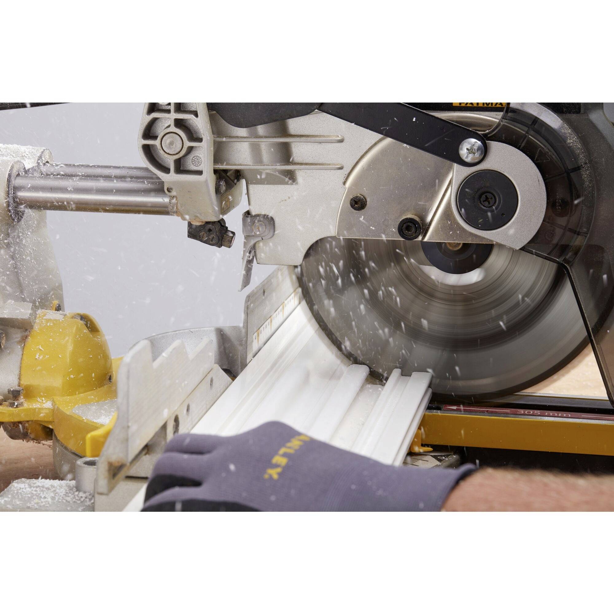 Eine Kappsäge schneidet präzise ein weißes Stück Holz. Funken fliegen und eine Person hält das Holz mit einer behandschuhten Hand fest.