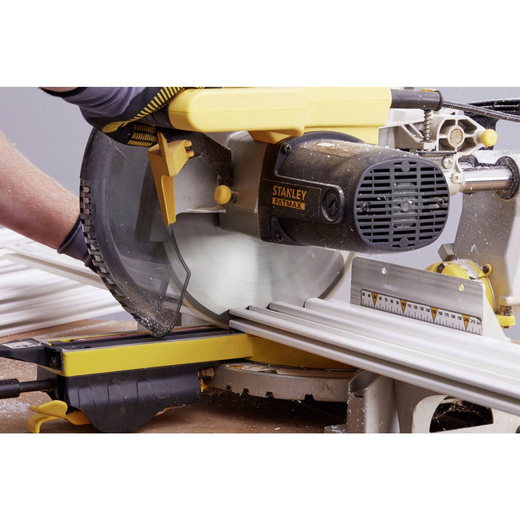 Eine Person schneidet mit einer elektrisch betriebenen Kappsäge ein langes weißes Brett. Die Säge ist schwarz-gelb.