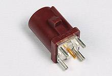 Ein roter, zylindrischer elektrischer Steckverbinder mit mehreren metallischen Stiften, platziert auf einer weißen Oberfläche.