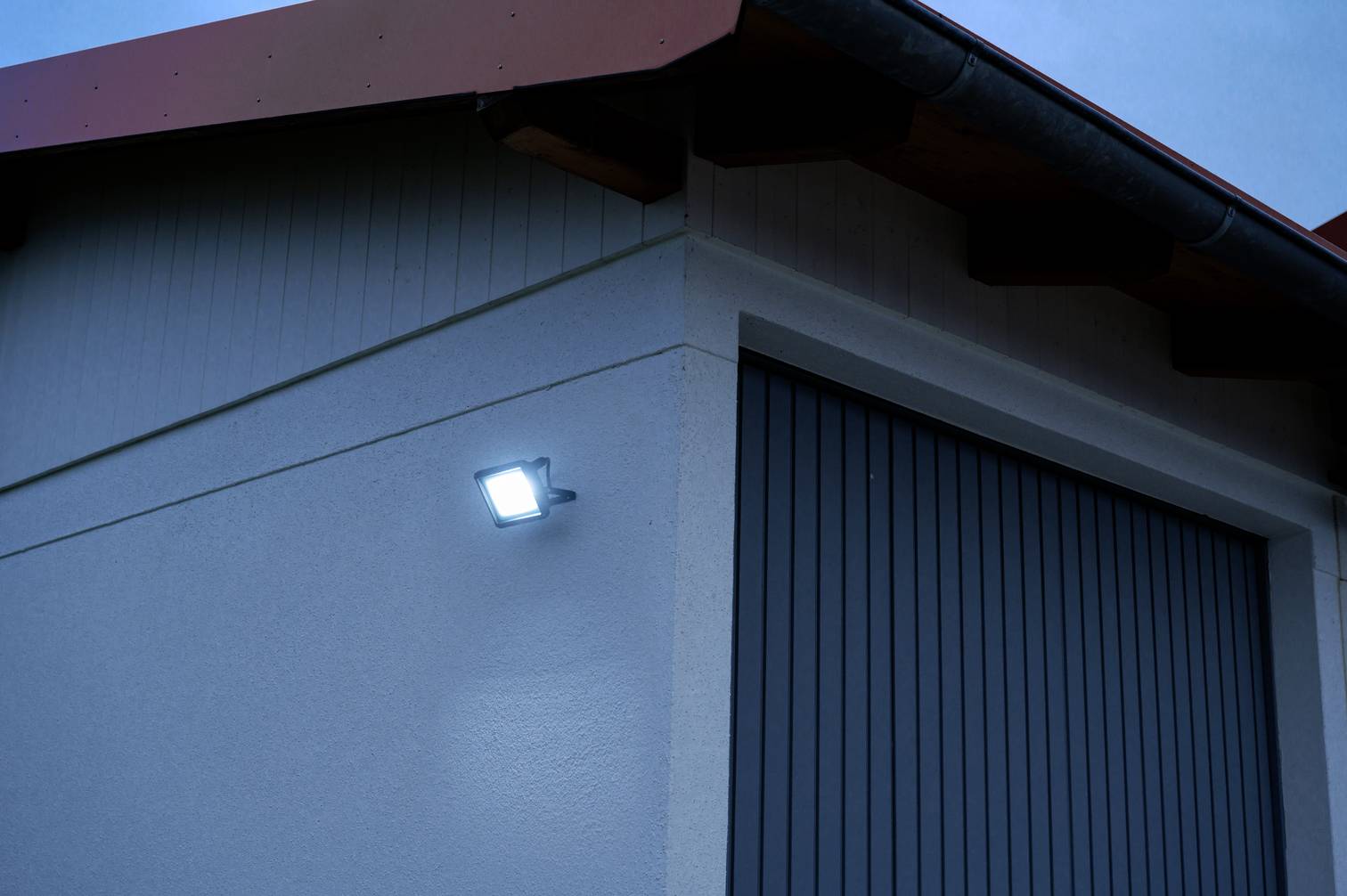 Außenansicht eines Gebäudes bei Dämmerung. An der Wand leuchtet ein heller LED-Strahler, der das Gebäude beleuchtet.