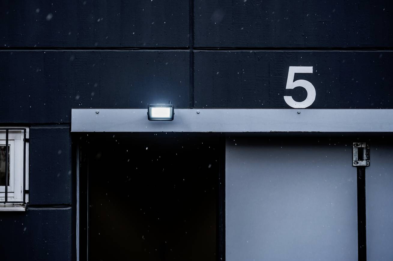 Tür zu einem dunklen Raum mit der Nummer 5 oben rechts. Ein Außenlicht leuchtet über dem Eingang. Schneeflocken fallen leicht.
