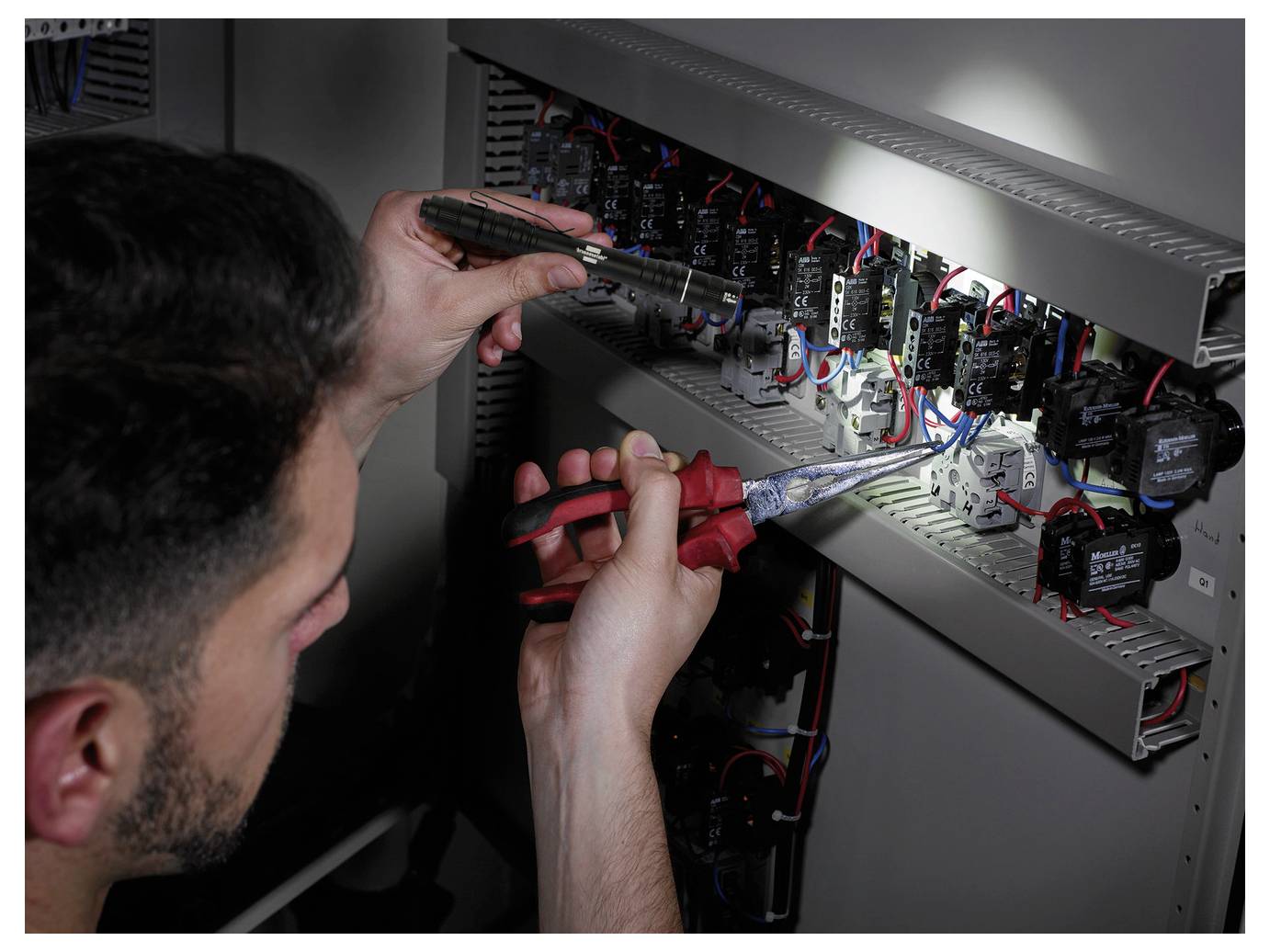 Techniker verdrahtet und inspiziert ein elektrisches Bedienfeld mit Schraubendreher und Zange, umgeben von Relais, Schaltern und Kabeln.