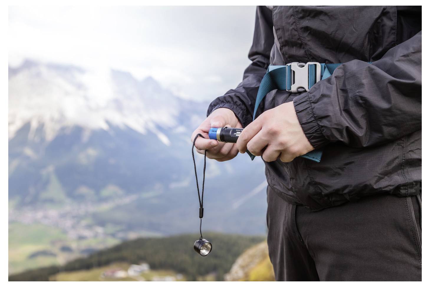 Nahaufnahme eines Wanderers, der einen Kompass an einem Umhängeband hält, mit verschwommenen Bergen im Hintergrund.