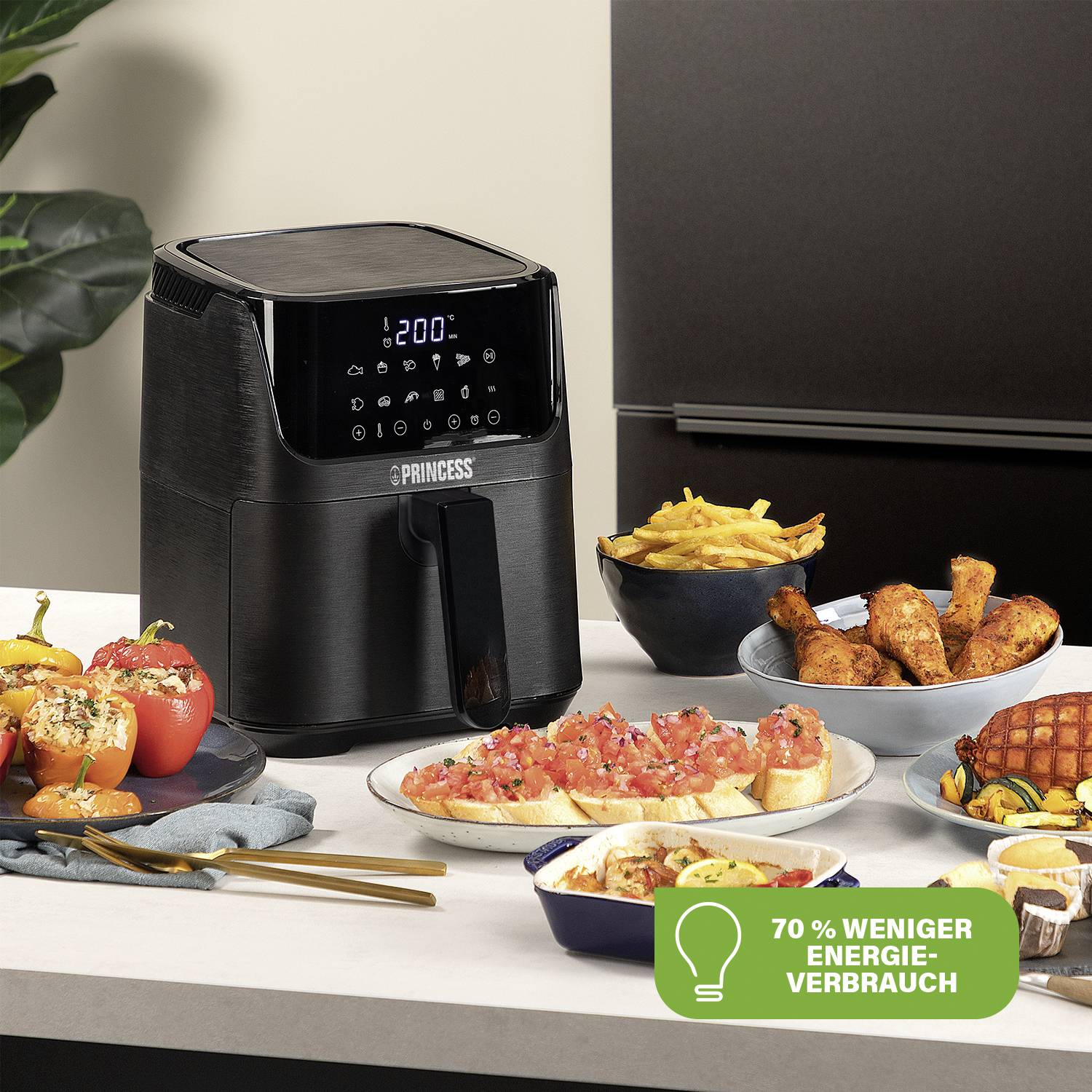 Eine schwarze Heißluftfritteuse auf einem Tisch neben verschiedenen Speisen. Ein Badge zeigt '70 % weniger Energieverbrauch'.