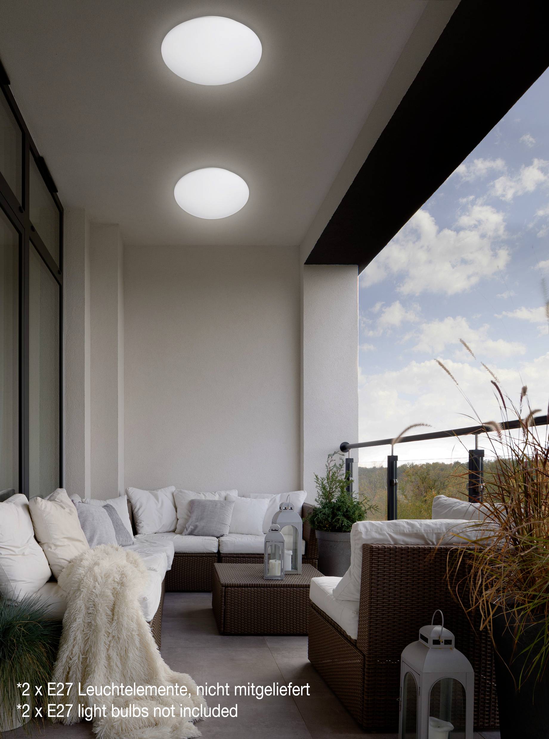 Ein Balkon mit gemütlicher Sitzgruppe, dekoriert mit Pflanzen. Über dem Sofa hängen zwei runde Deckenleuchten.