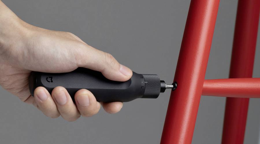 Eine Hand hält einen schwarzen, elektrischen Schraubendreher und zieht eine Schraube in einem roten Möbelstück an.