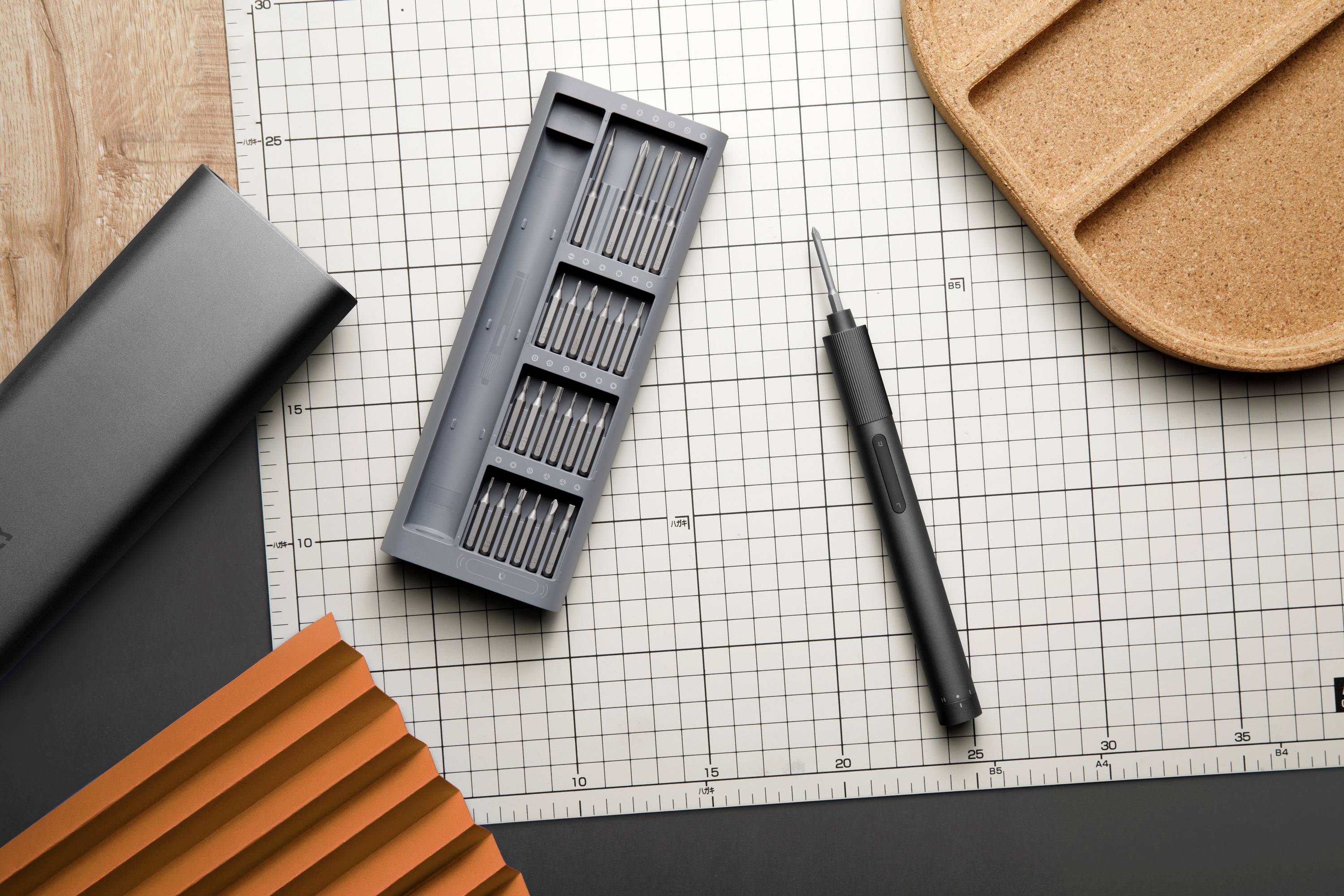 Werkzeugset auf kariertem Hintergrund. Enthält einen magnetischen Schraubendreher mit verschiedenen Aufsätzen und eine braune Ablage.