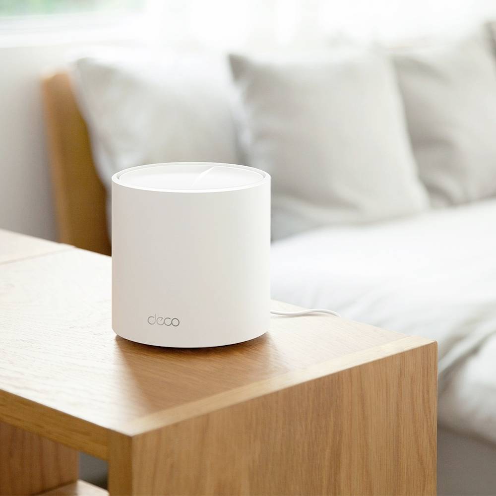 Ein zylindrisches, weißes Gerät steht auf einem Holztisch vor einem Sofa. Es handelt sich um einen WLAN-Router.