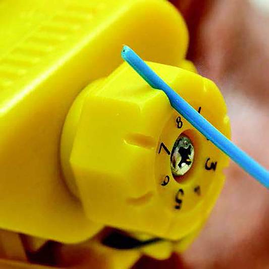 Ein gelber Drehknopf auf einer Maschine, beschriftet mit Zahlen 0 bis 5. Ein blauer Stab zeigt auf die Zahl 4.