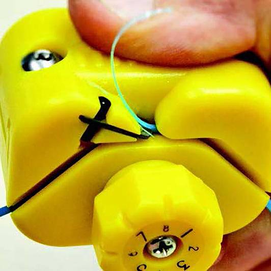 Nahaufnahme einer gelben, handgehaltenen Vorrichtung, die Draht spannt. Fokus auf einem nummerierten Einstellrad und einer Fingerhaltung.