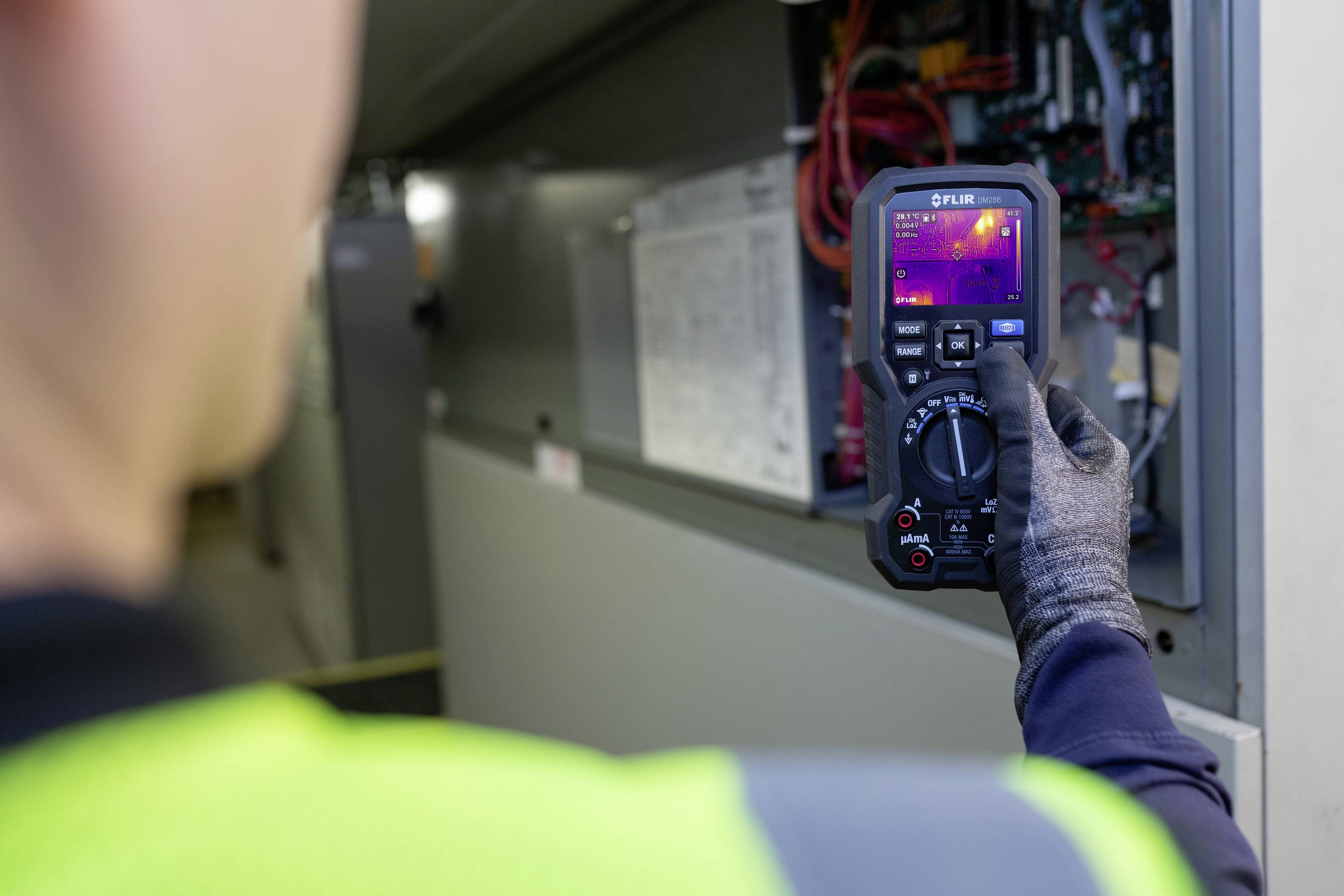 Ein Techniker in Schutzkleidung überprüft mit einer Wärmebildkamera die elektrischen Komponenten eines Schaltschrankes.