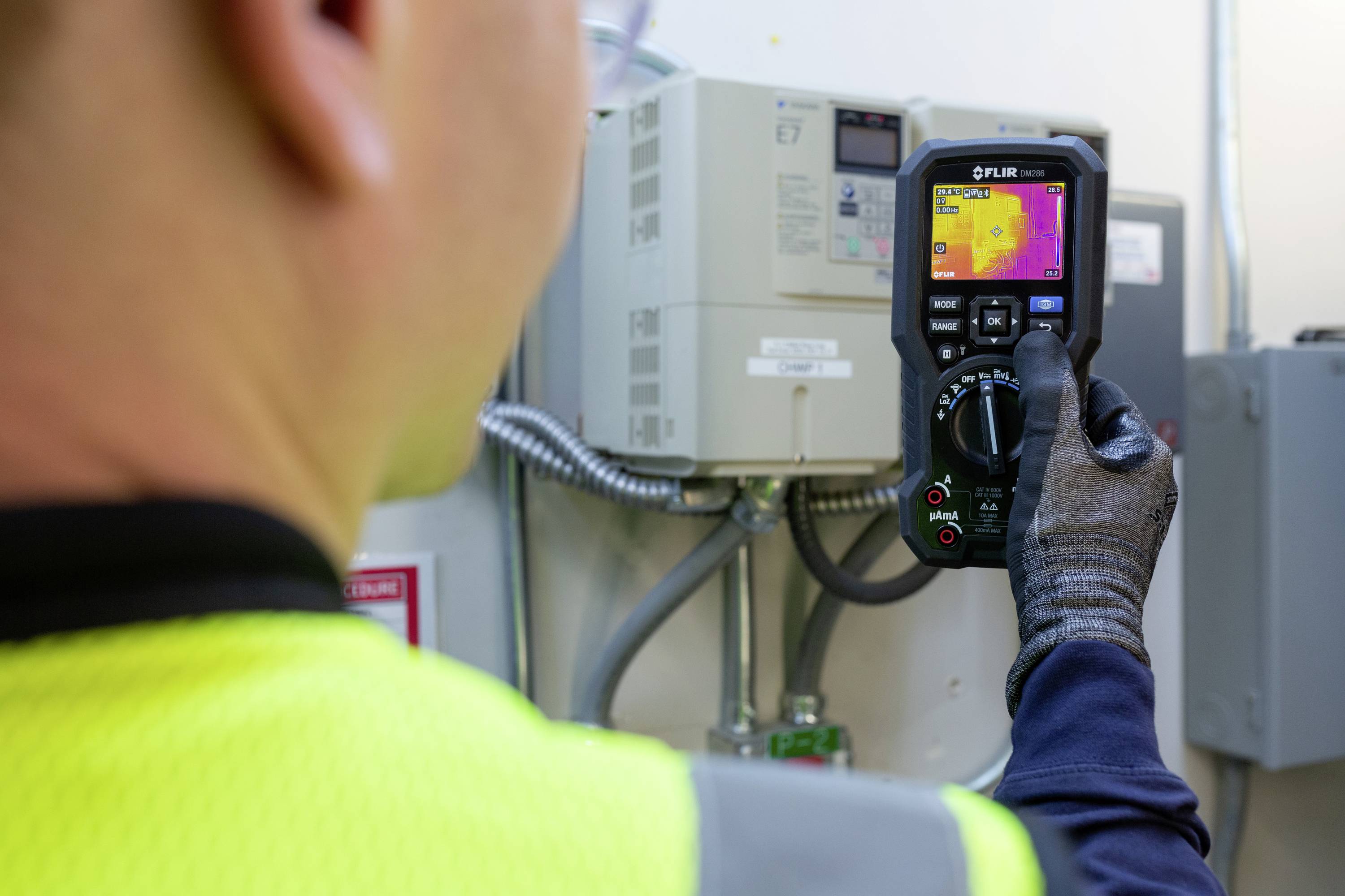 Eine Person in Sicherheitskleidung nutzt eine Wärmebildkamera, um die Temperatur eines elektrischen Geräts zu überprüfen.