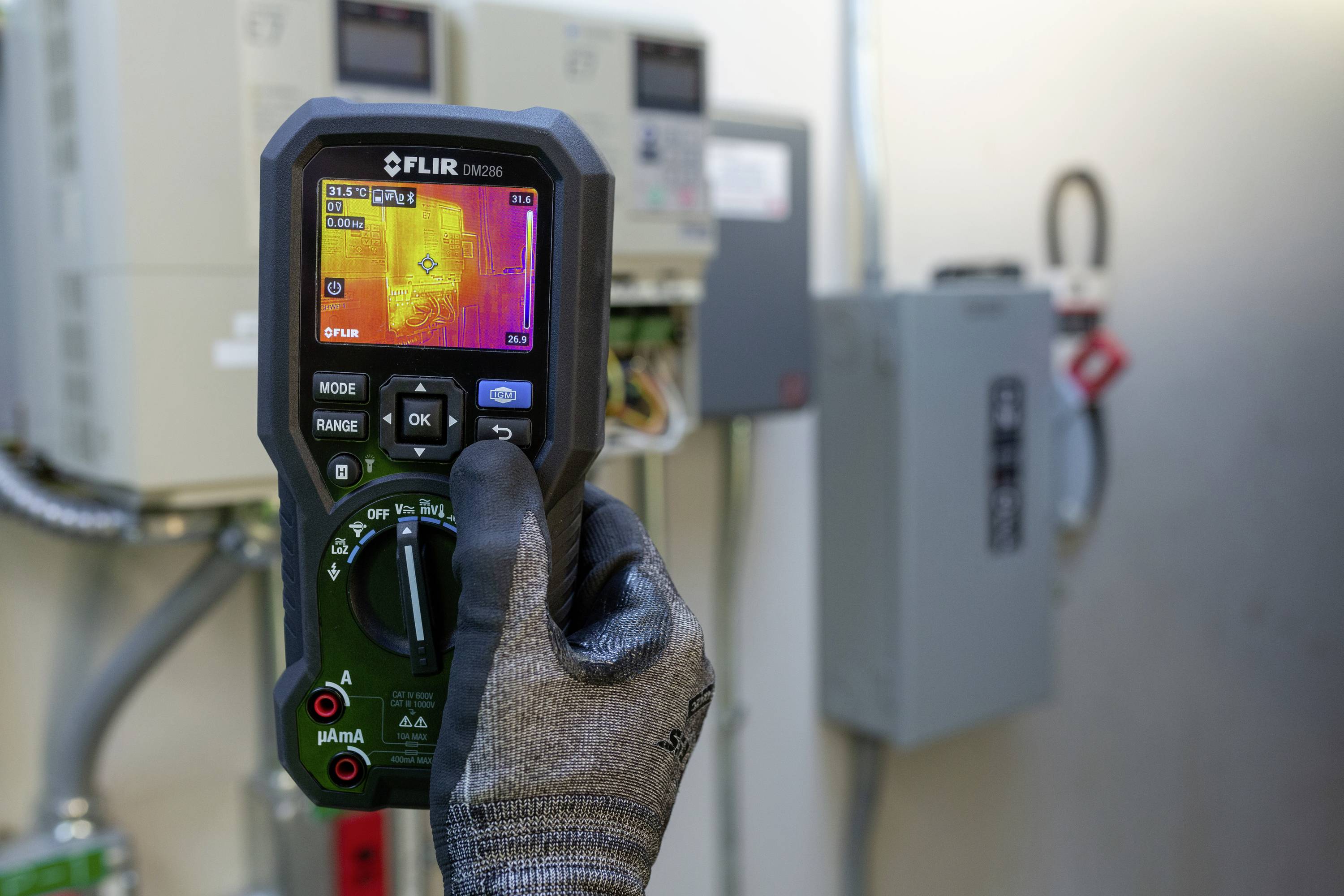 Eine Person hält ein Wärmebildkamera-Gerät vor elektrischen Schaltkästen. Auf dem Bildschirm ist Hitzeverteilung zu sehen.