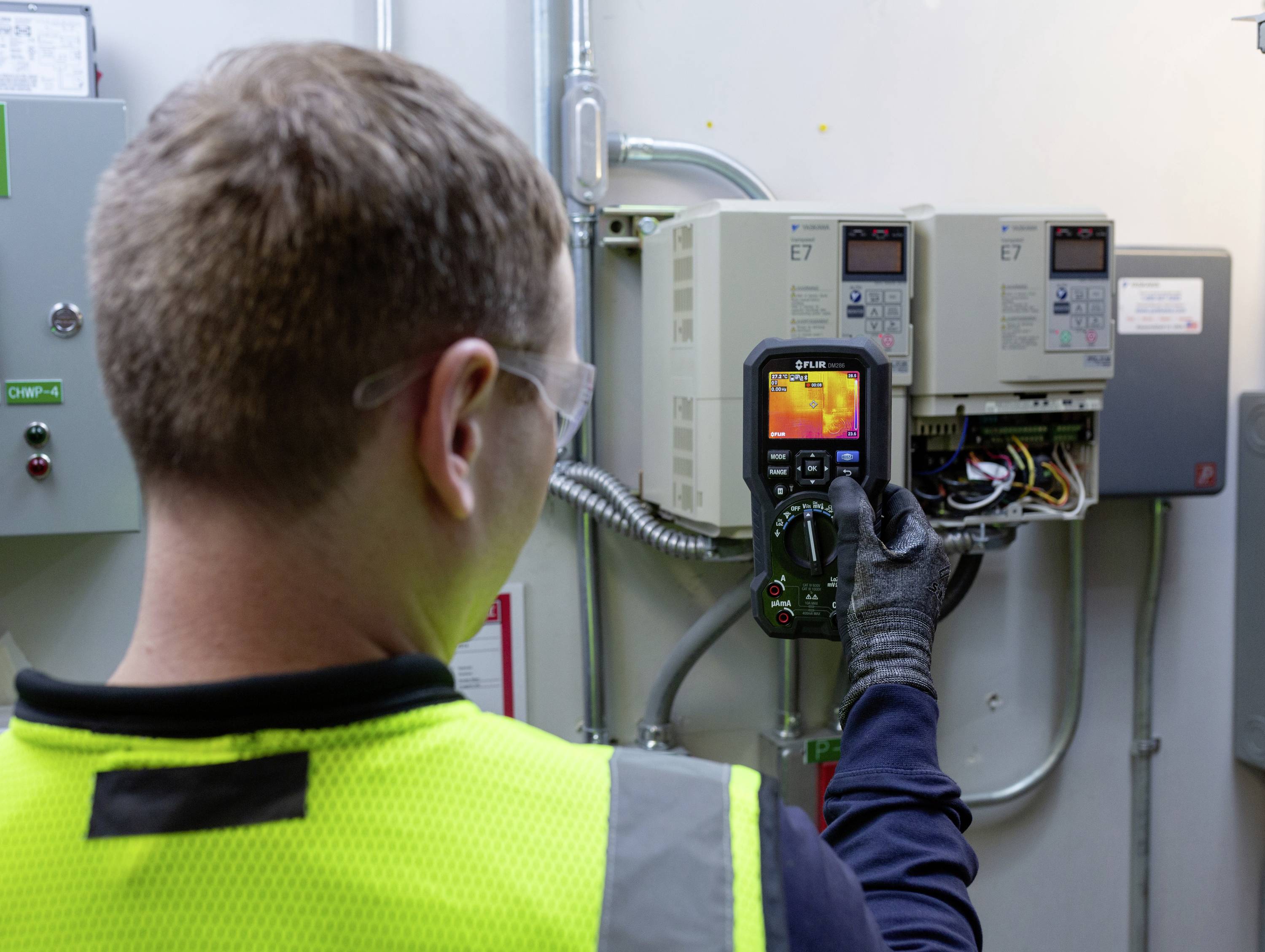 Ein Techniker verwendet ein Infrarot-Thermometer zur Überprüfung elektrischer Steuergeräte in einem Wartungsraum.