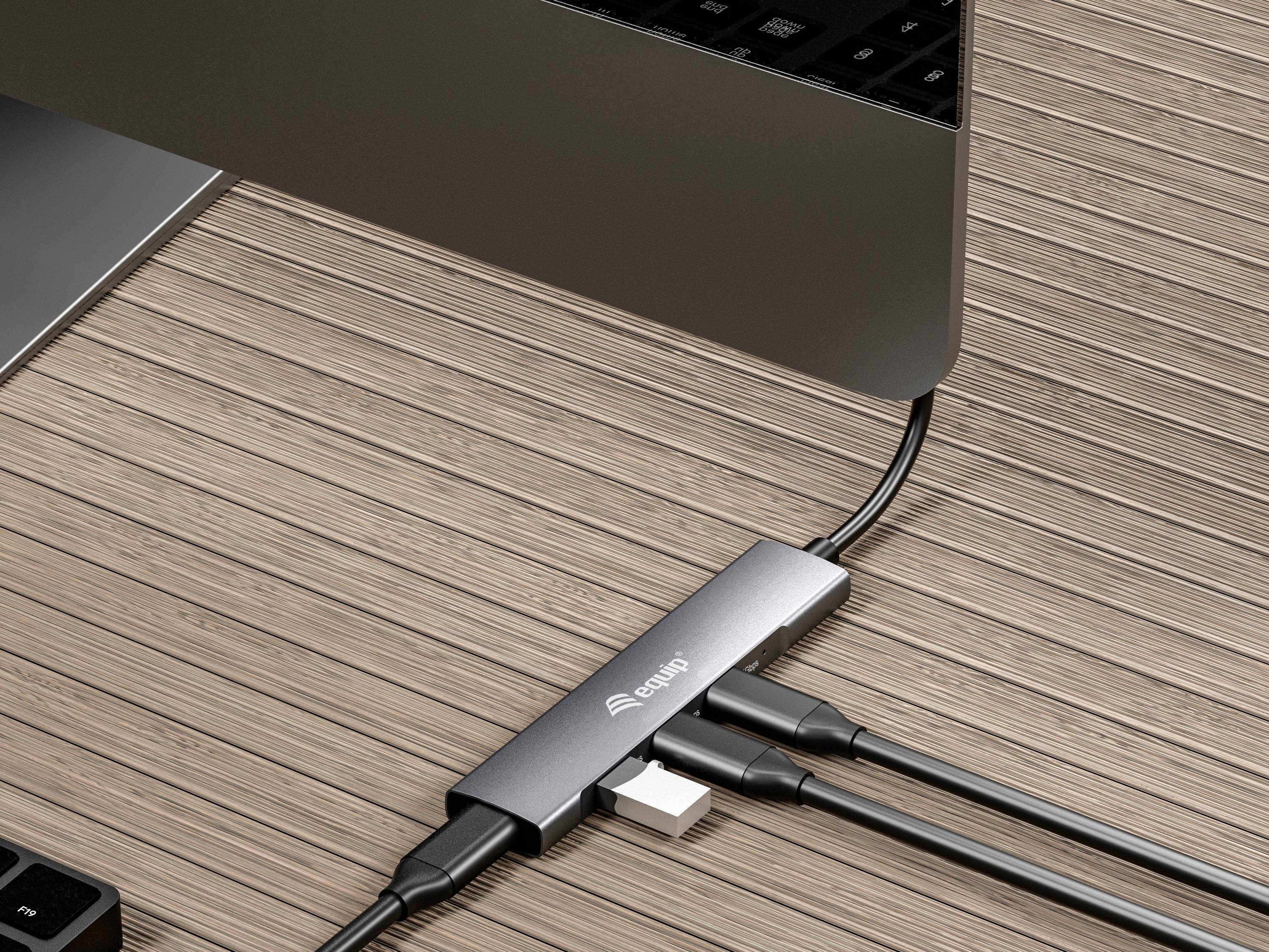 Ein Laptop steht auf einem Holztisch, verbunden mit einem USB-Hub, der mehrere Kabel aufnimmt. Der Fokus liegt auf der Anschlussvielfalt.