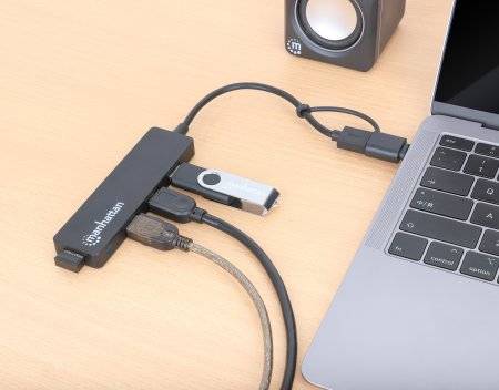 Mehrfachanschlussgerät verbindet Laptop über USB-C mit USB-Stick, HDMI-Kabel und Netzteil. Lautsprecher im Hintergrund.