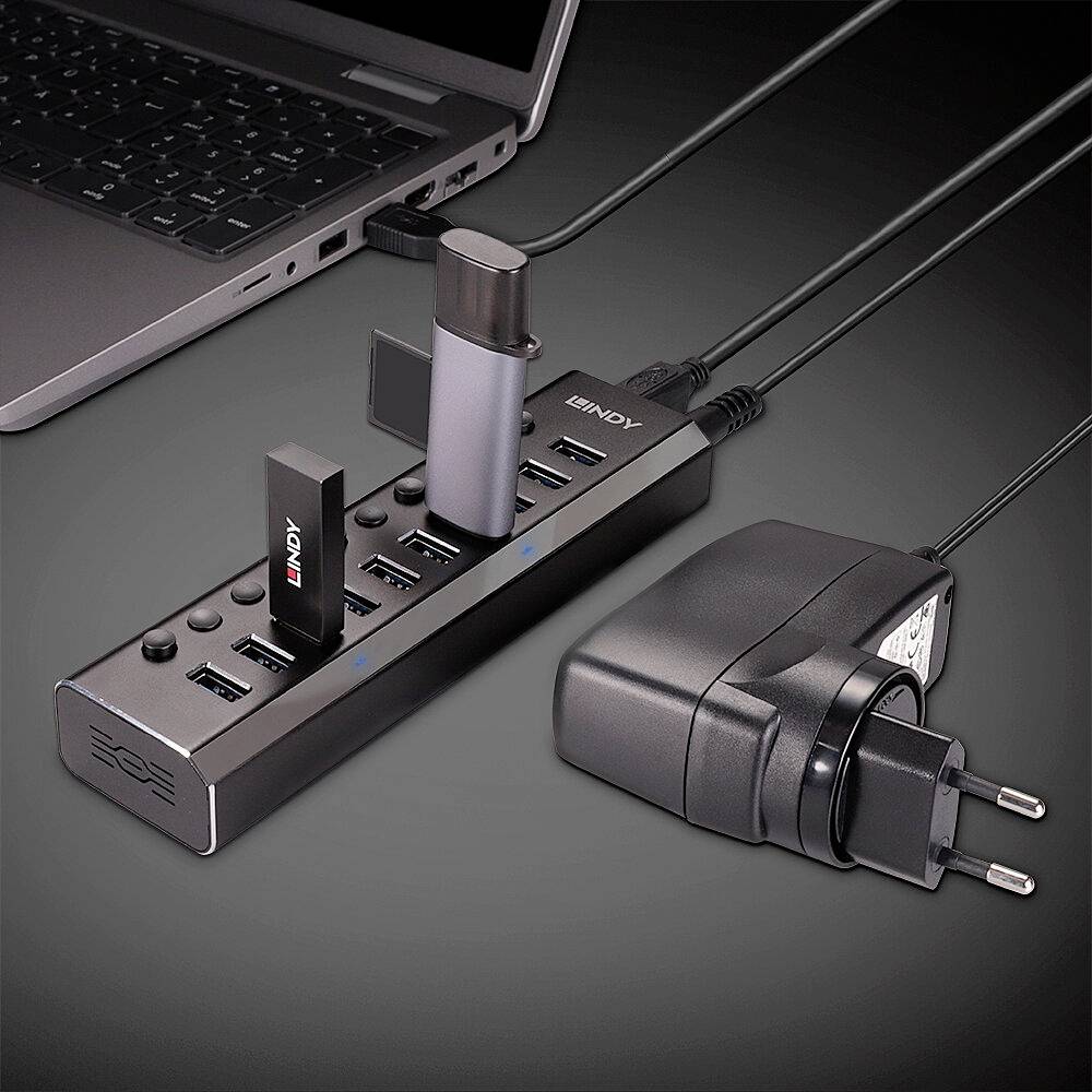 USB-Hub mit acht Anschlüssen, verbunden mit einem Laptop. Zwei Geräte sind eingesteckt. Ein Netzadapter liegt daneben.