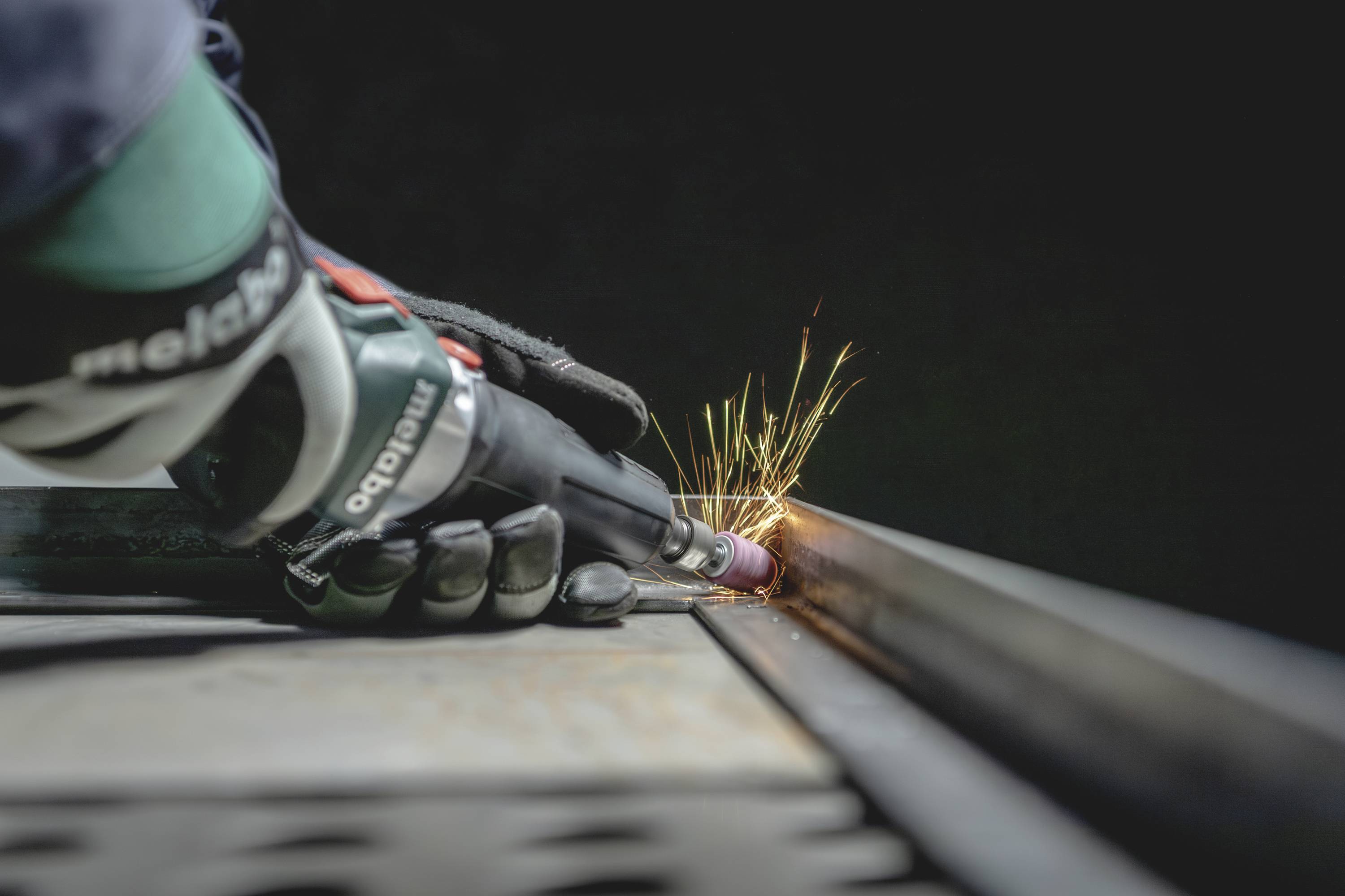 Die Nahaufnahme zeigt eine Person, die mit Schutzhandschuhen ein Metallstück schleift, während Funken sprühen.