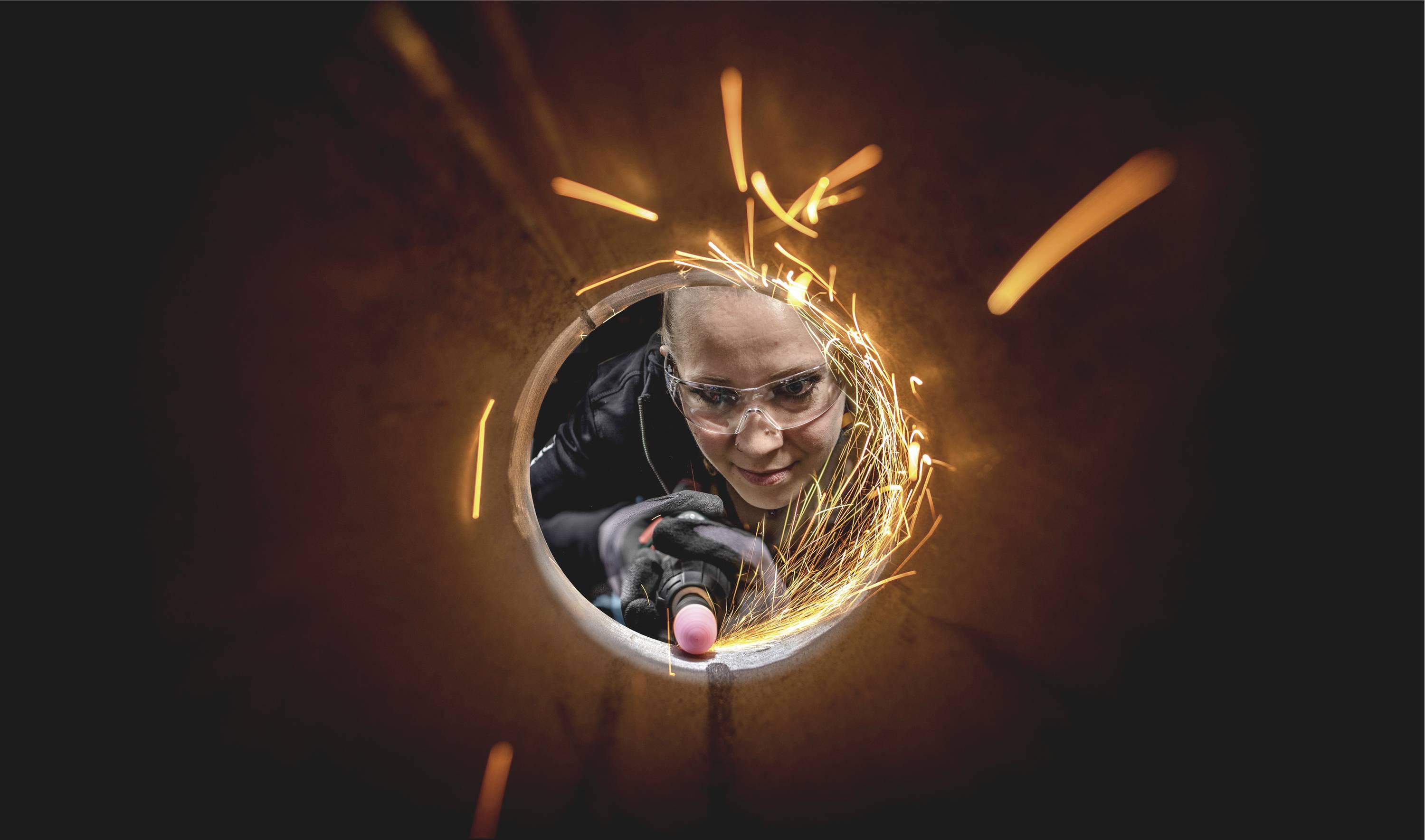 Eine Person trägt eine Schutzbrille und benutzt ein Schweißgerät. Funken sprühen im Tunnel, während sie konzentriert arbeitet.