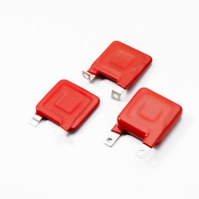 Drei rote elektronische Kondensatoren mit flachem rechteckigen Gehäuse, auf weißem Hintergrund, zwei liegend, einer stehend.