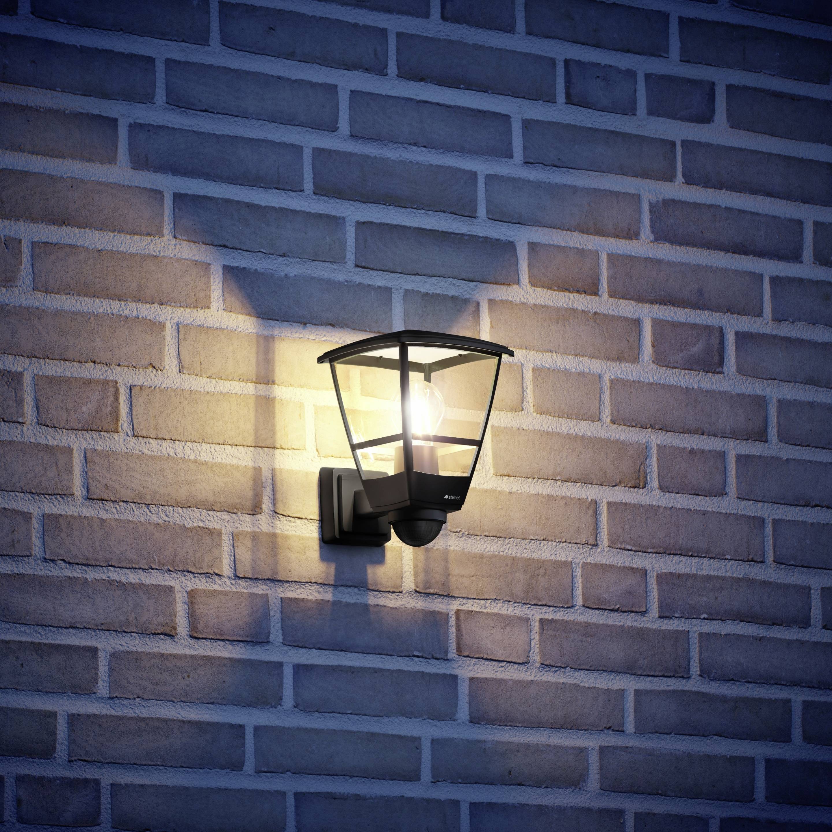 Außenlampe an einer Backsteinwand im Dunkeln beleuchtet, erzeugt einen warmen Lichtschein auf die Wand.