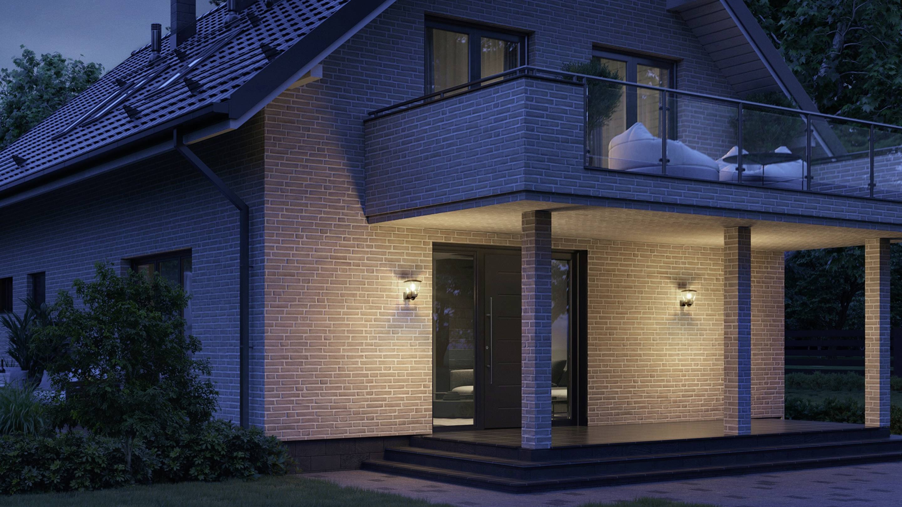 Ein modernes Einfamilienhaus bei Nacht, beleuchtet von Außenlampen, mit Balkon und Dachschräge, umgeben von Bäumen.