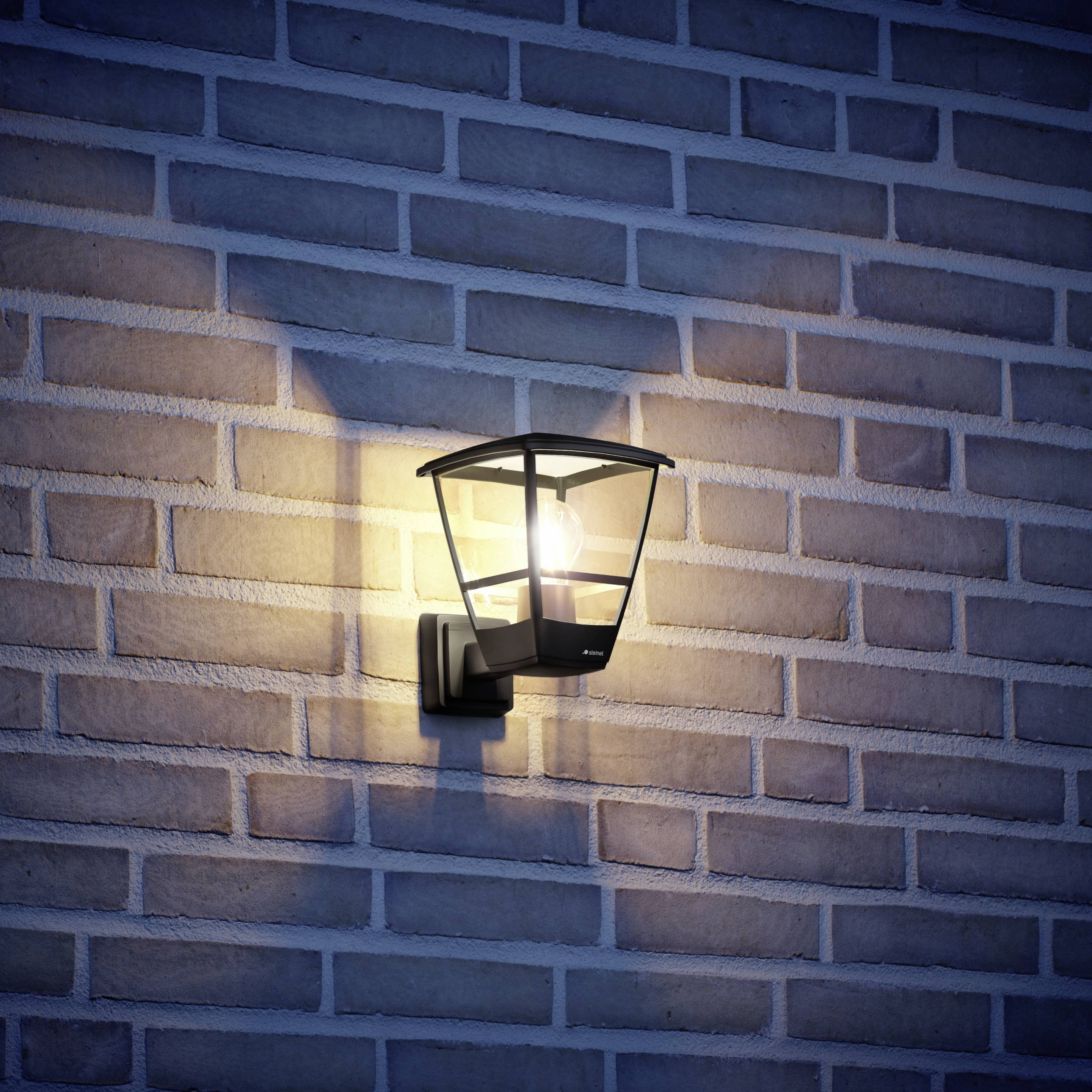 Wandleuchte an Backsteinwand, leuchtet warmes Licht in der Dämmerung.