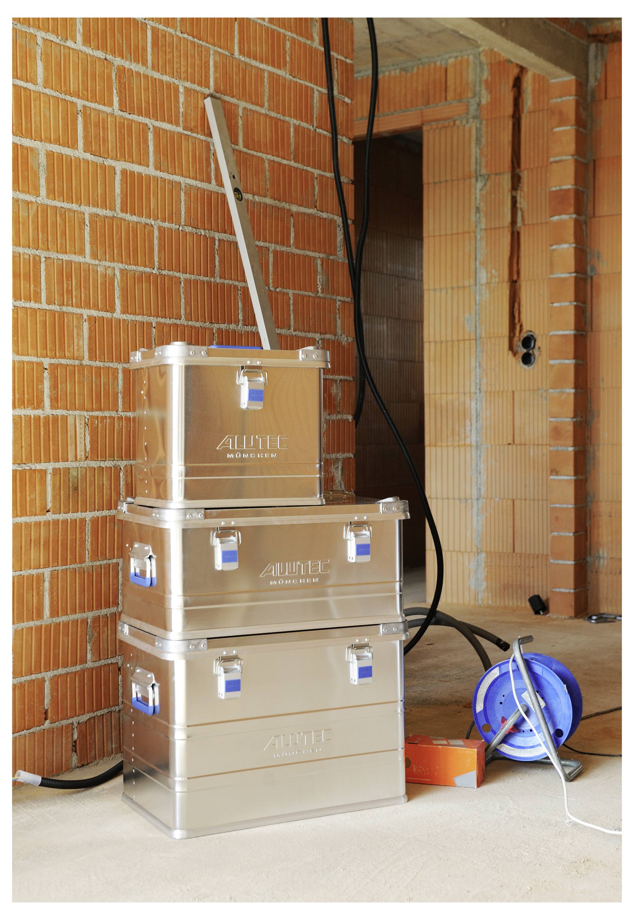 Drei übereinander gestapelte Metalllagerkästen mit Griffen und Verschlüssen, die sich in einem teilweise fertiggestellten Raum mit sichtbaren Backsteinwänden und Stromleitungen befinden.