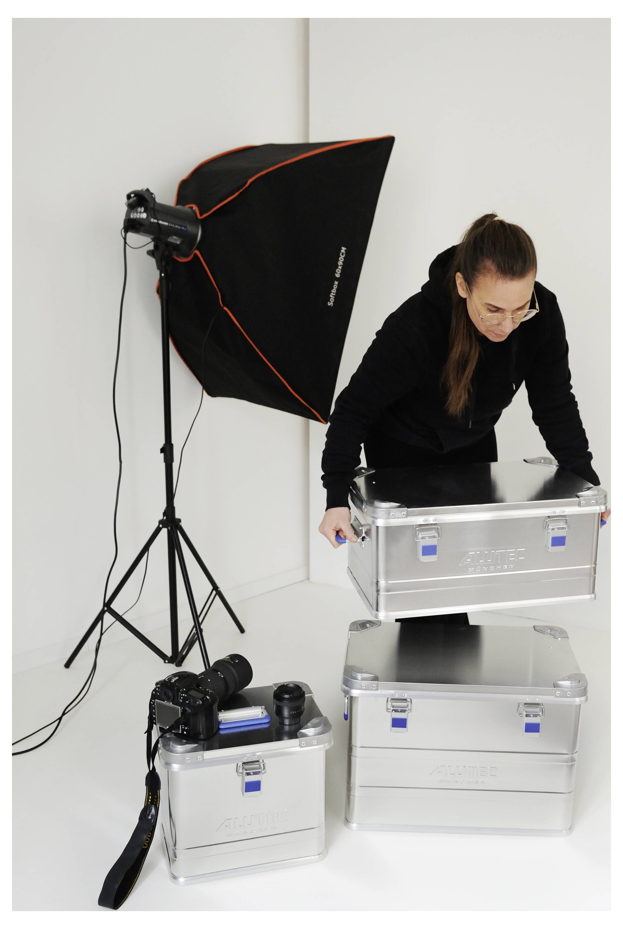 Person, die Metallboxen neben fotografischem Beleuchtungs- und Kameraequipment in einer Studioumgebung stapelt.