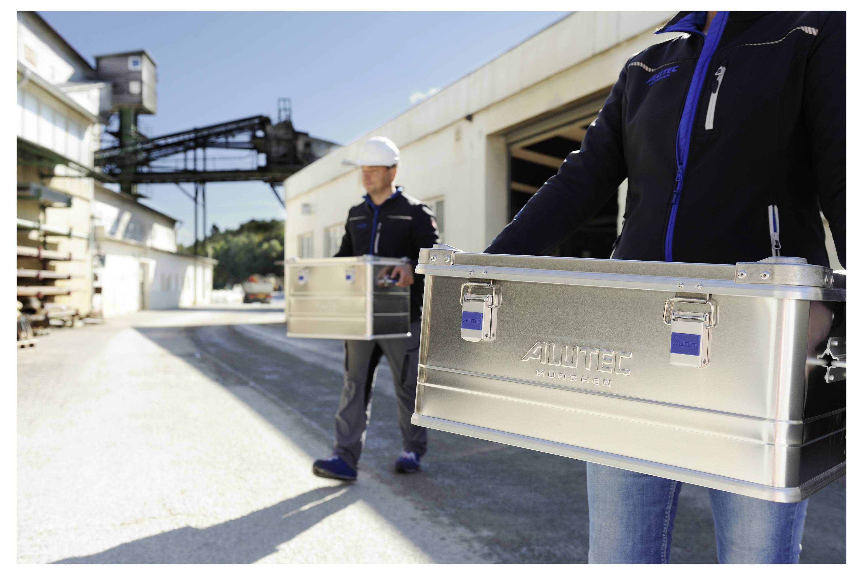 Zwei Personen tragen metallische Werkzeugkästen mit der Aufschrift 