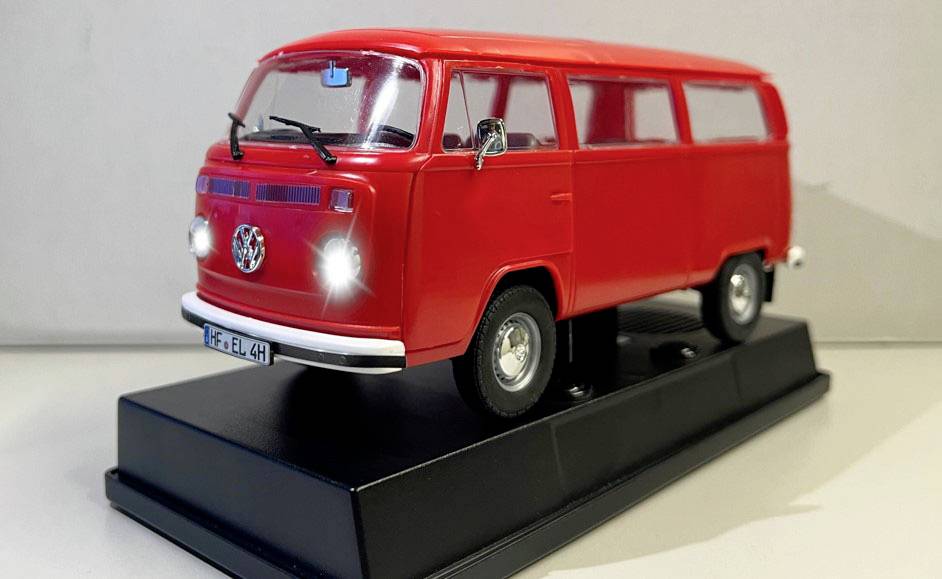 Rotes Modellauto eines klassischen VW Transporters, auf einem schwarzen Sockel präsentiert.