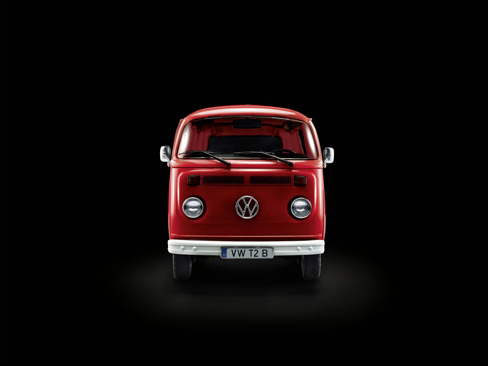 Roter Volkswagen-Bus T2, Frontalansicht auf schwarzem Hintergrund. Der Bus hat runde Scheinwerfer und ein markantes VW-Logo.