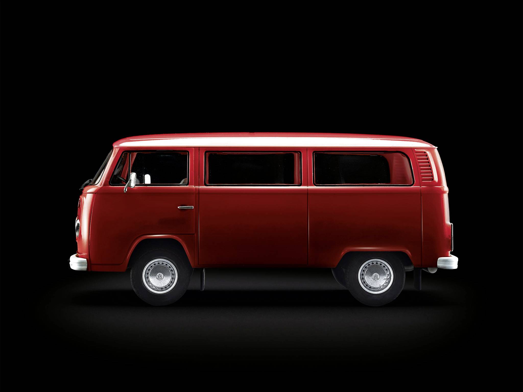 Ein roter VW-Bus der Modelle der 1970er Jahre auf schwarzem Hintergrund, von der Seite gesehen.