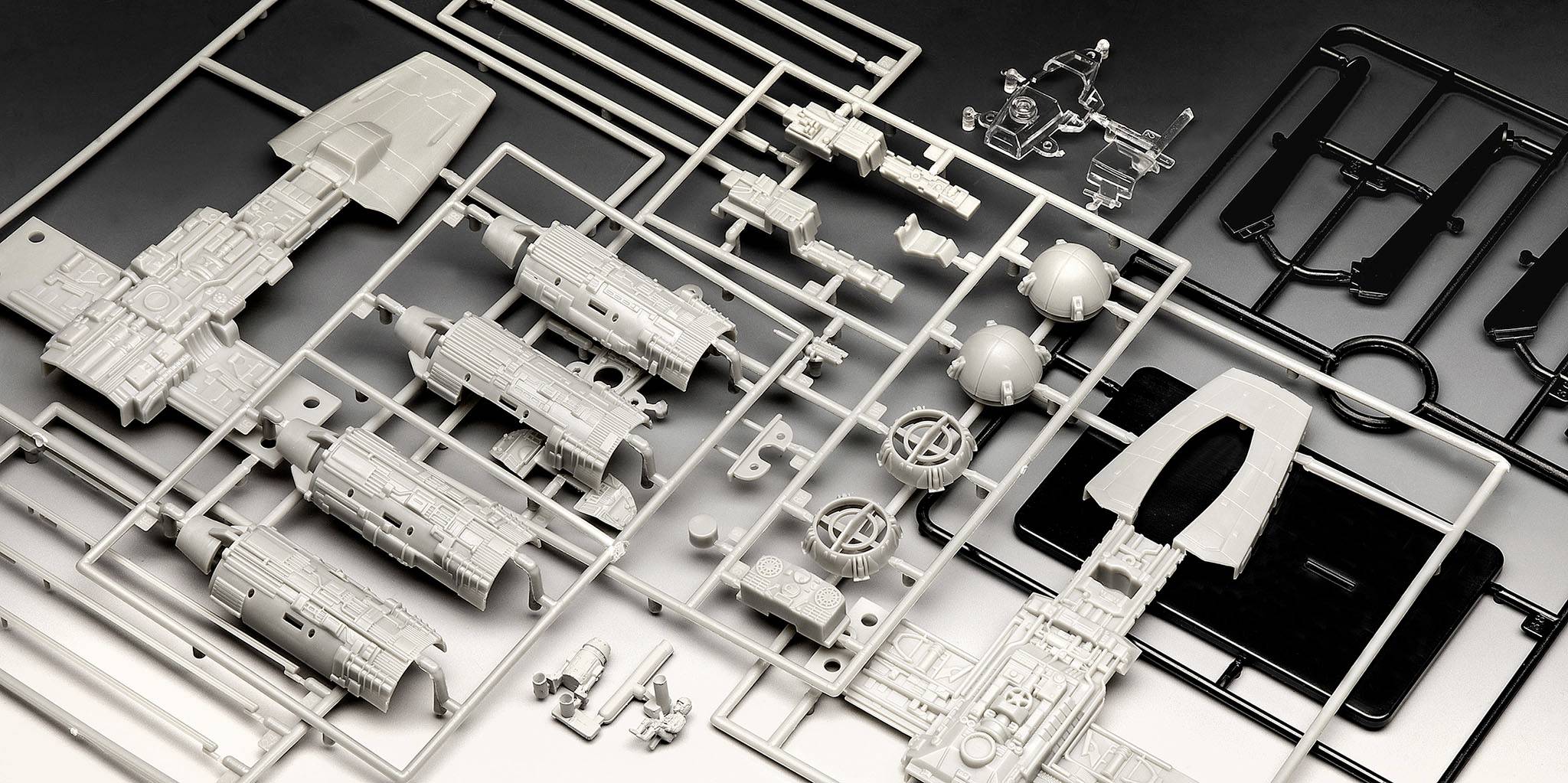 Plastikbausatz mit Einzelteilen eines Raumschiffs auf einem Tisch. Die Komponenten sind in verschiedenen Formen und Größen angeordnet.