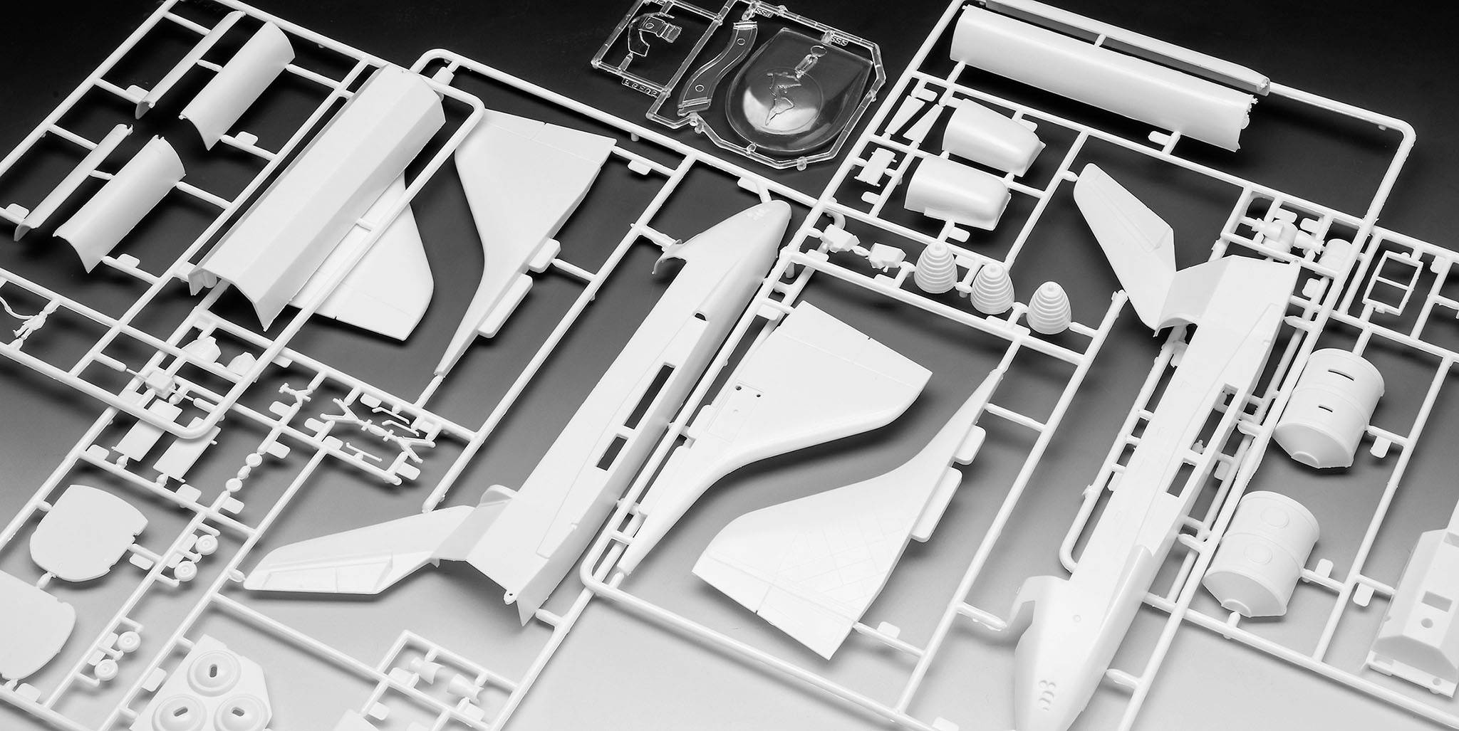 Bausatz für ein Modellflugzeug aus weißem Kunststoff. Verschiedene Flugzeugteile sind in einem Gitterrahmen angeordnet.