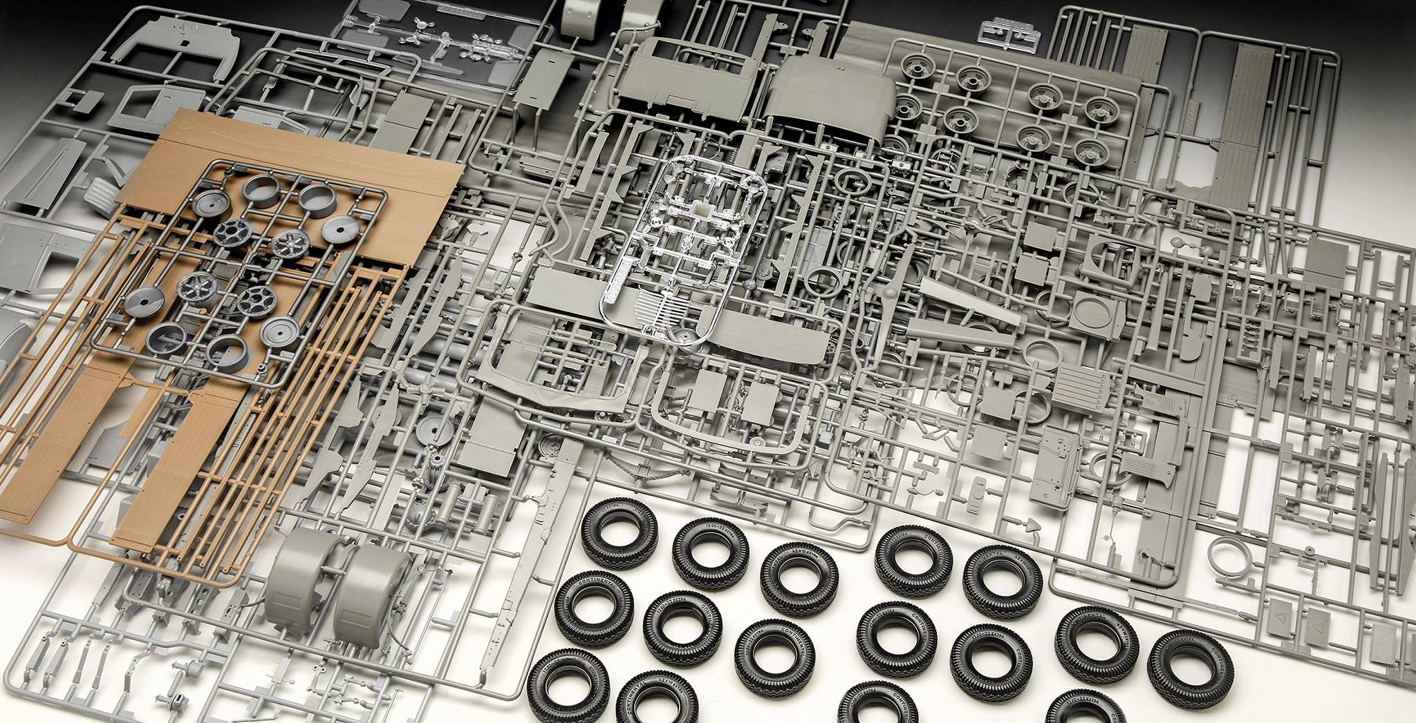Mehrere Modellbausätze liegen ungeordnet auf einer Fläche. Es sind Räder, Rahmen und diverse Bauteile erkennbar.