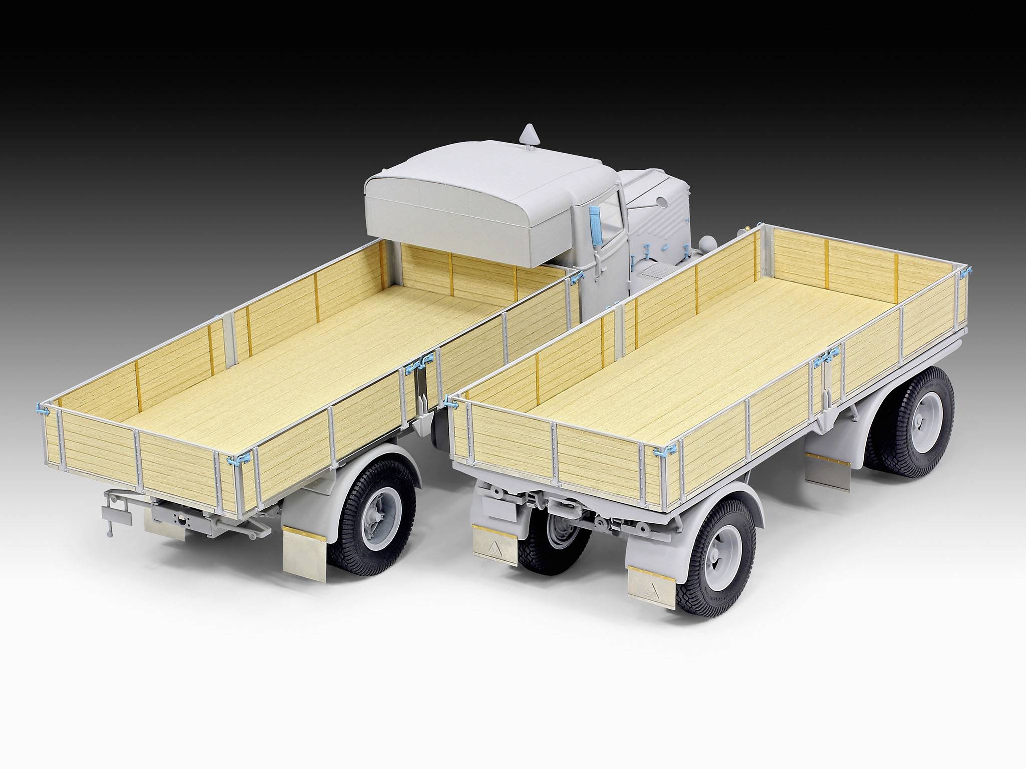 Zwei Modell-Lkw-Anhänger, grau mit Holzdetails, stehen nebeneinander auf einer Fläche. Sie sind unmontiert und detailreich gestaltet.