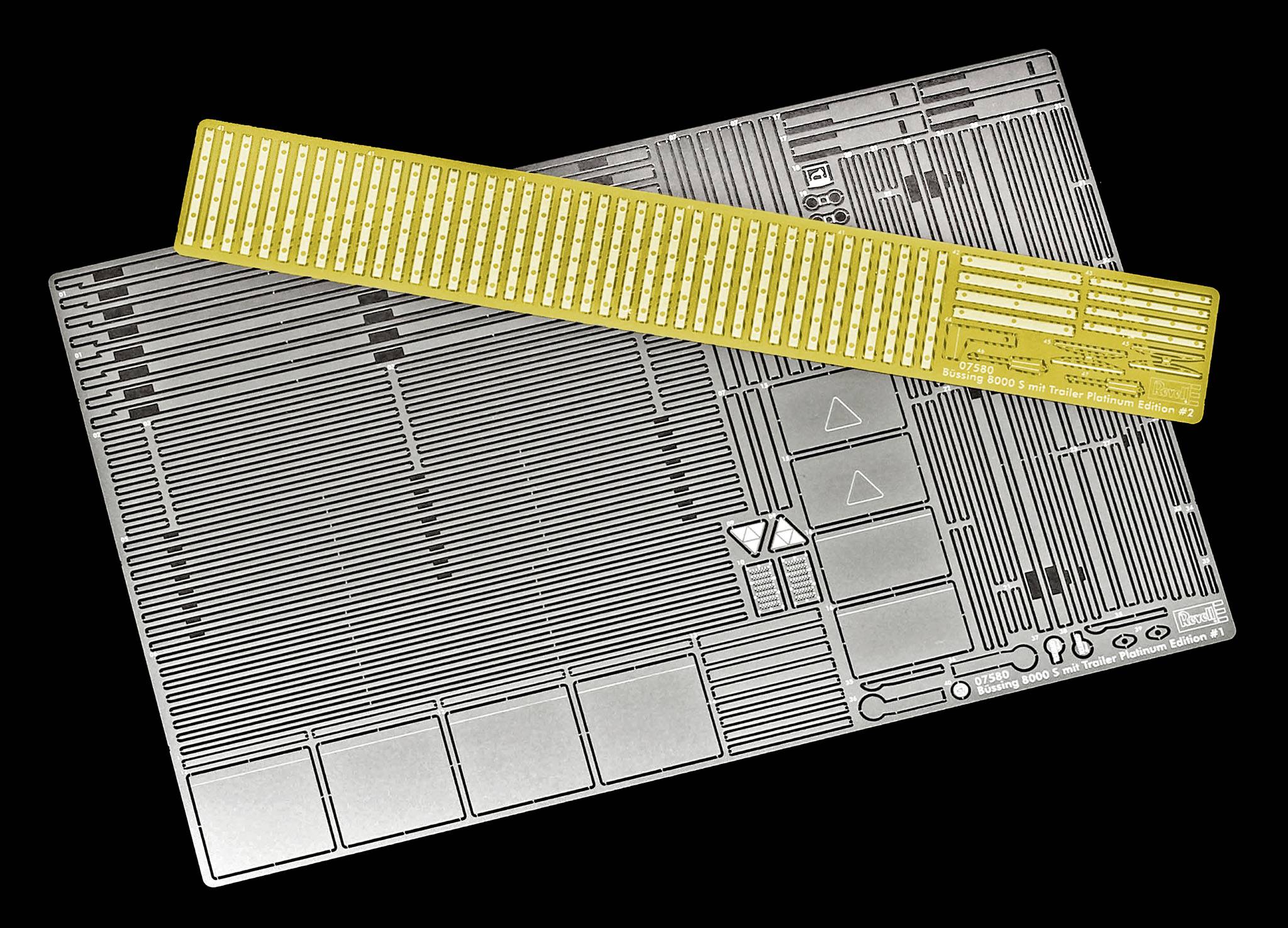Ein silbernes Modellbau-Set mit kleinen, detaillierten Teilen auf schwarzem Hintergrund. Ein goldener Maßstab liegt diagonal darauf.