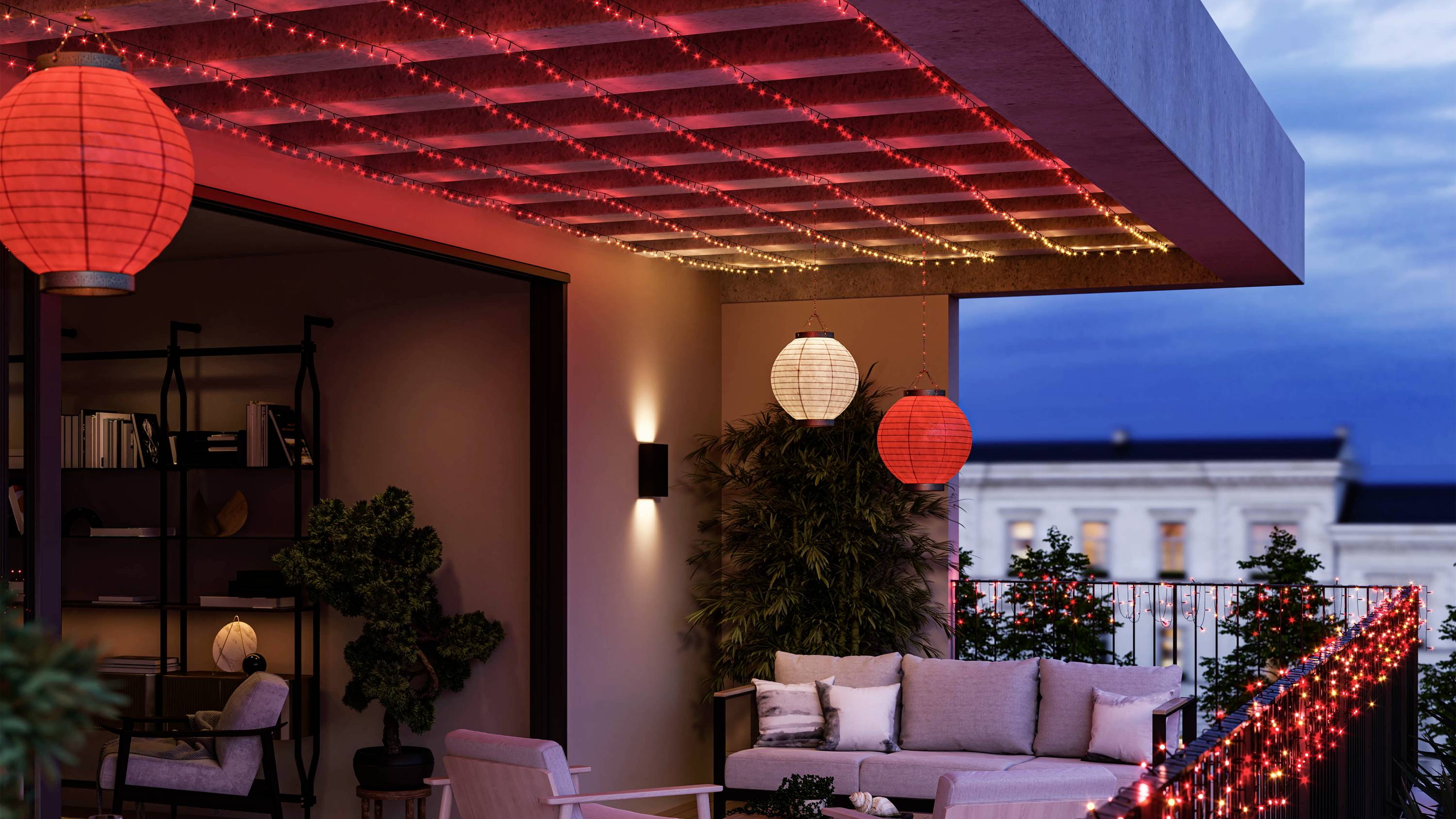 Ein Balkon bei Dämmerung mit gemütlicher Sitzgruppe, dekorativen roten Laternen und Lichterketten. Hintergrund zeigt einen beleuchteten Himmel.