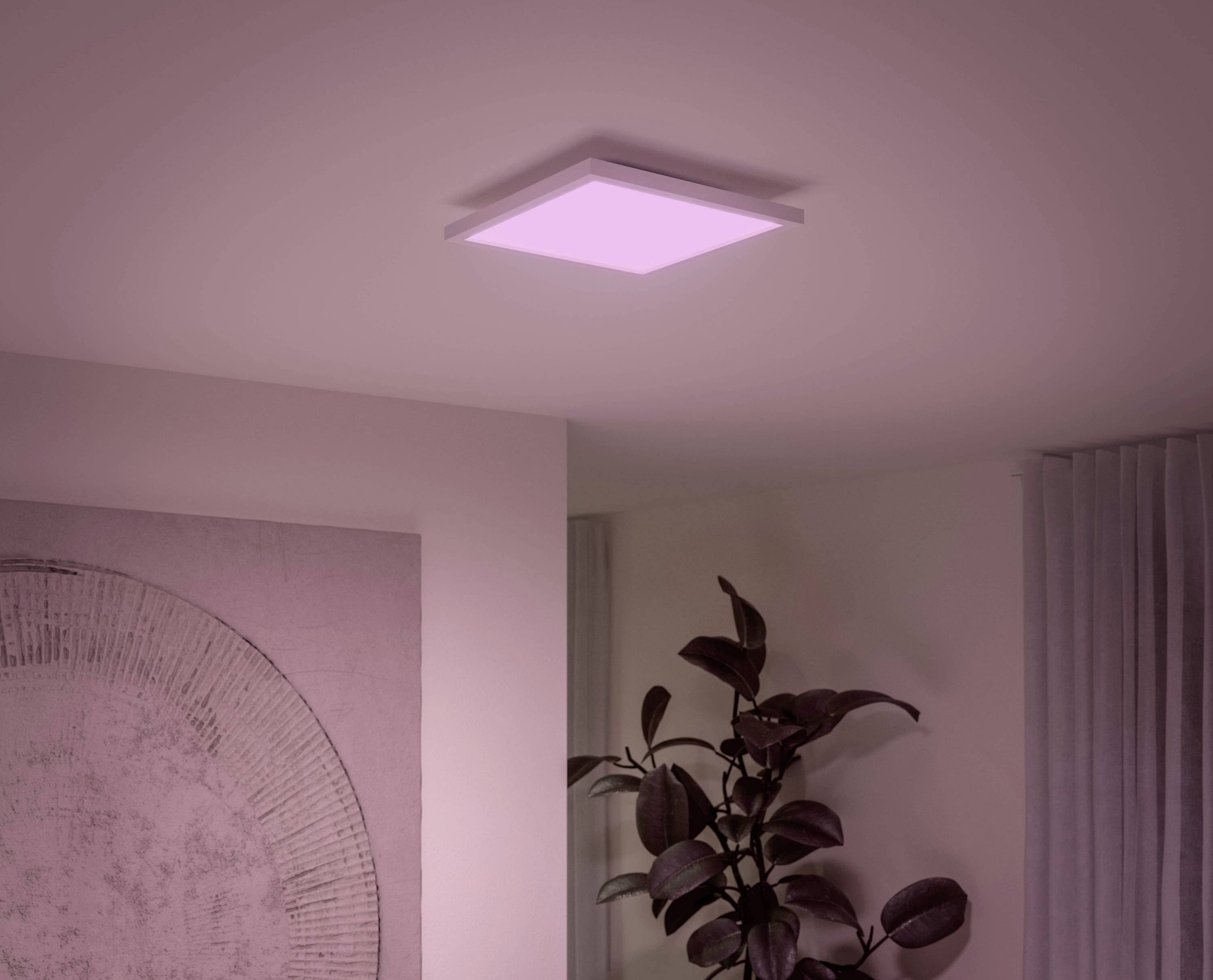 Eine quadratische Deckenleuchte, die weiches rosa Licht abgibt, beleuchtet eine Zimmerdecke. Eine Pflanze steht daneben.