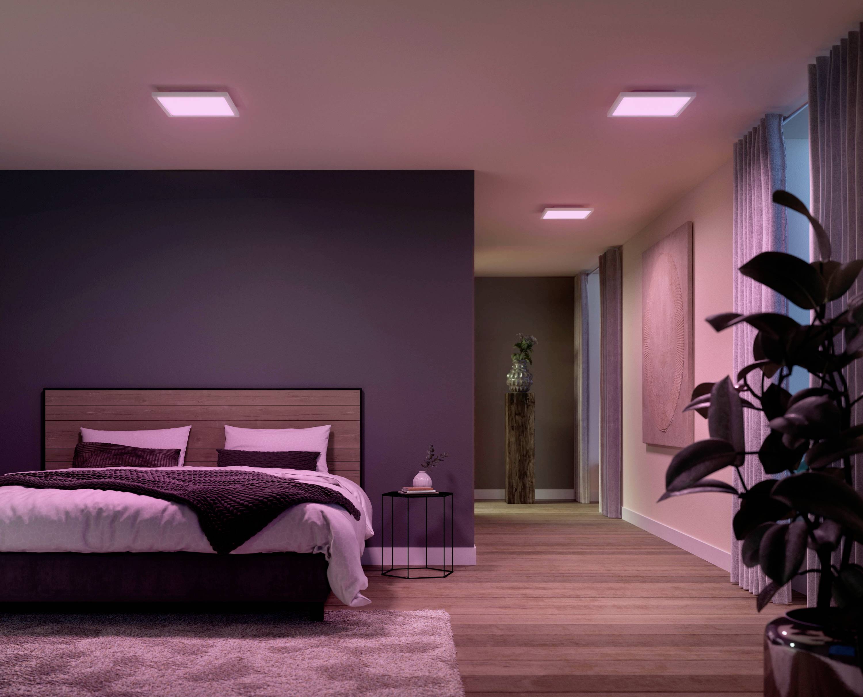 Ein modern eingerichtetes Schlafzimmer mit beleuchtetem Deckenlicht. Ein großes Bett steht links neben einem kleinen runden Tisch mit Kerze.