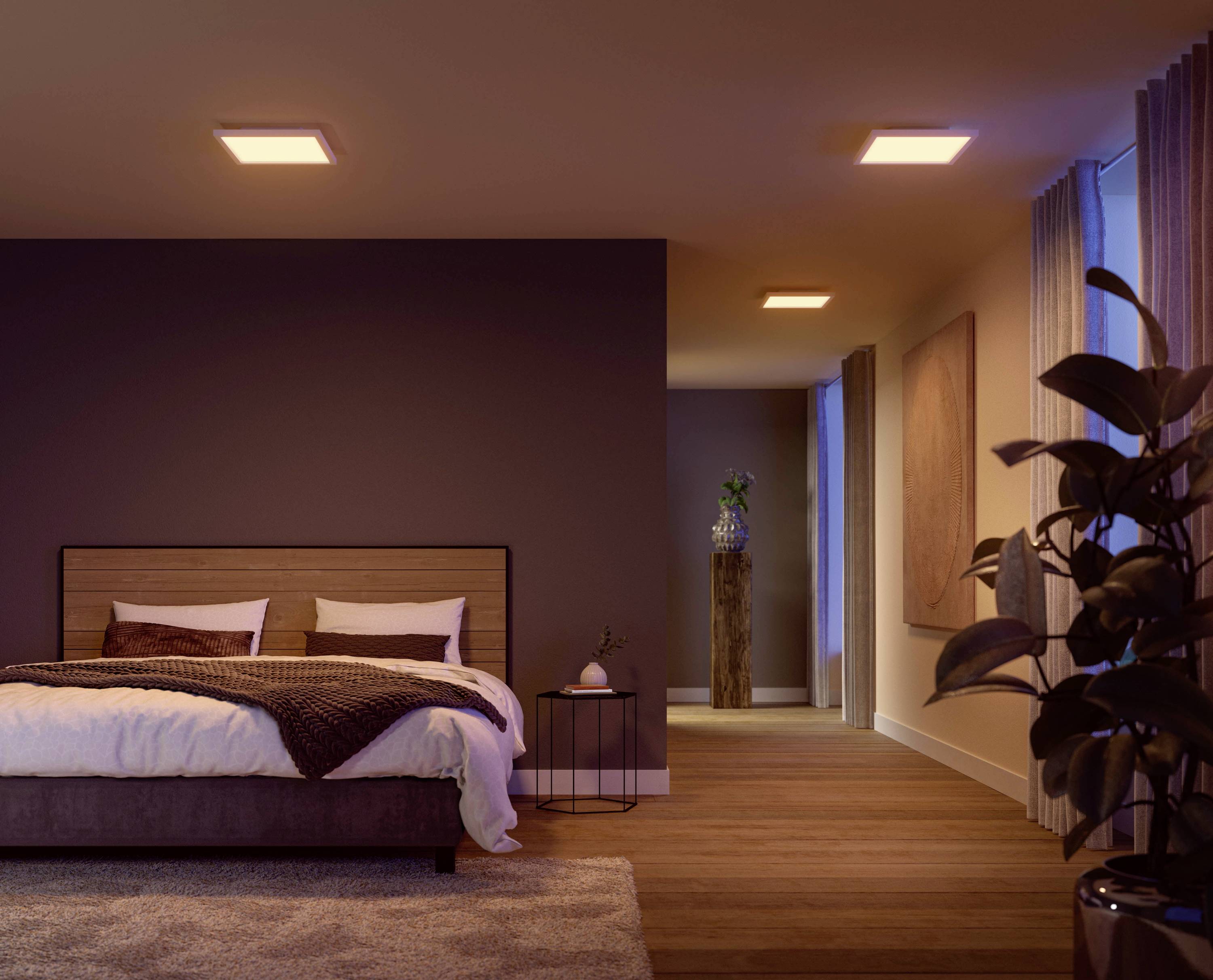 Schlafzimmer mit Doppelbett links, gemütlich beleuchtet, Teppichboden, Pflanze rechts, langer Flur führt zu einer offenen Tür hinten.