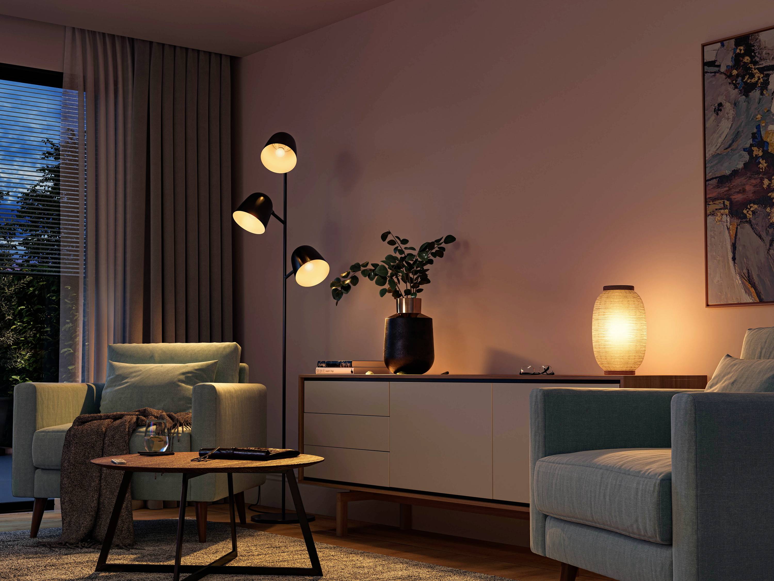 Wohnzimmer mit zwei Sesseln, Stehlampe, Couchtisch und Sideboard. Gedämpfte Beleuchtung schafft eine gemütliche Atmosphäre.