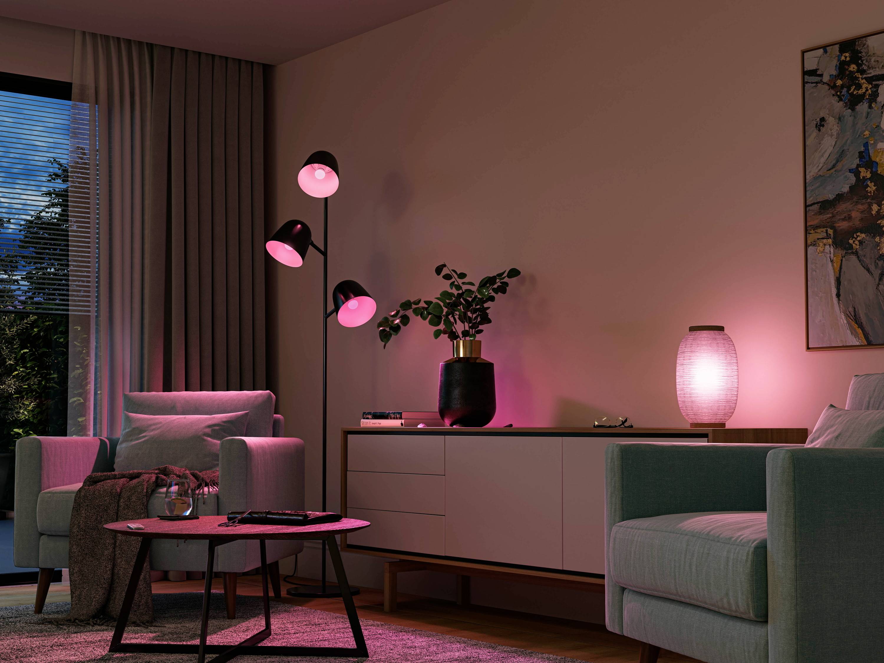 Gemütliches Wohnzimmer bei Dämmerlicht mit zwei Sesseln, Stehlampe, Kommode und Zimmerpflanze. Warmes, indirektes rosa Licht sorgt für eine entspannende Atmosphäre.