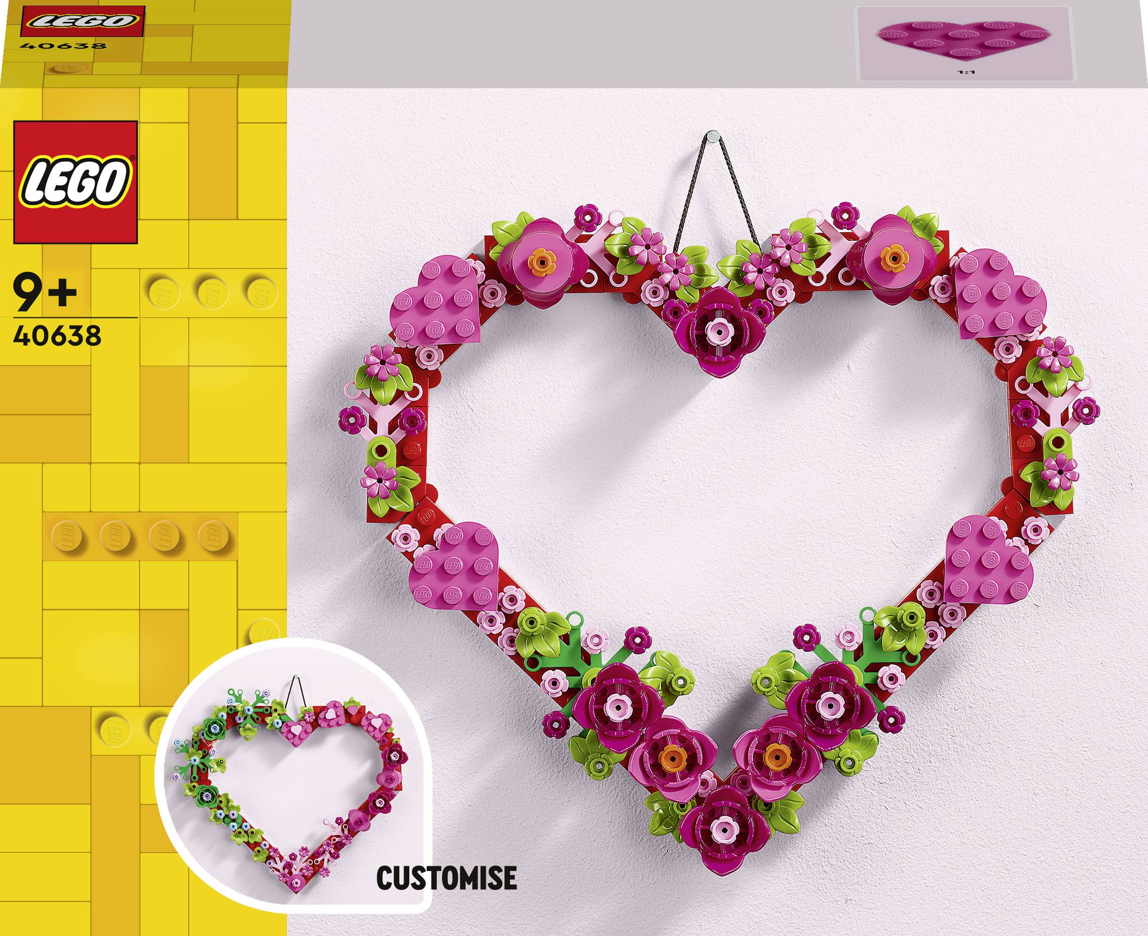 Ein herzförmiger Kranz aus LEGO-Steinen, verziert mit rosa und lila Blumen, für Kinder ab 9 Jahren geeignet.