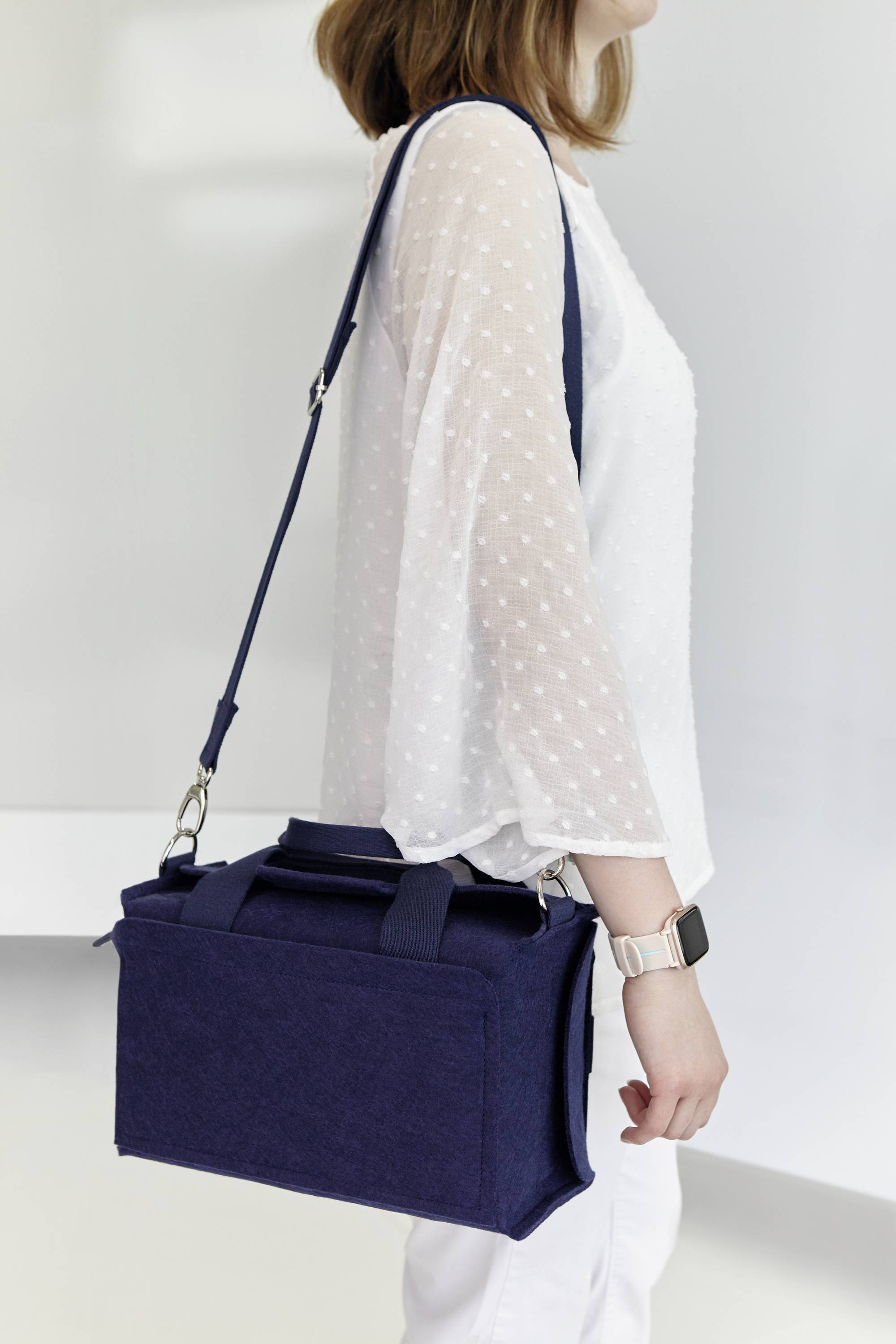Eine Person trägt eine dunkelblaue Umhängetasche. Sie trägt eine helle Bluse mit Punkten und eine Smartwatch.