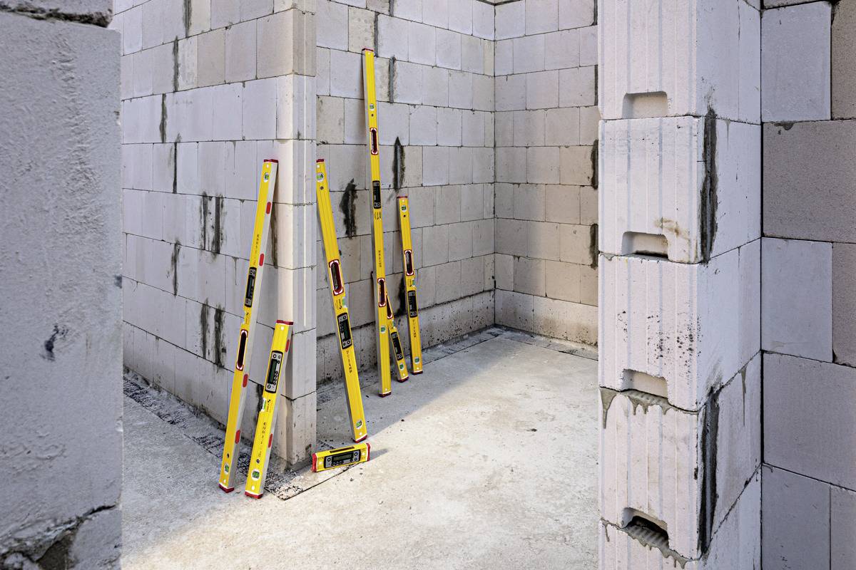 Eine Baustelle mit Ziegelwänden und vier gelben Wasserwaagen, die an den Wänden lehnen. Der Boden ist aus Beton.