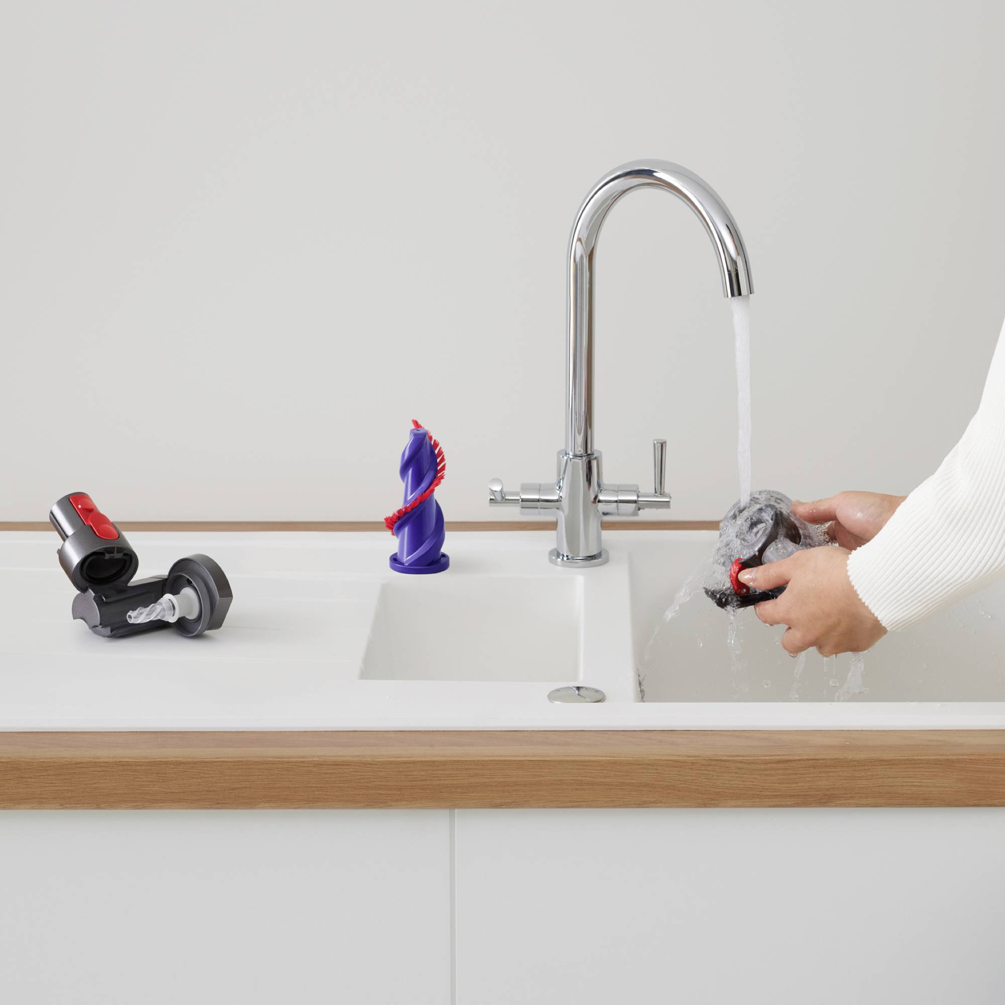 Arbeitsfläche mit Wasserhahn, aus dem Wasser fließt. Eine Hand hält einen grauen Schwamm unter dem Wasserstrahl. Links steht ein rot-schwarzer Schraubschlüssel.