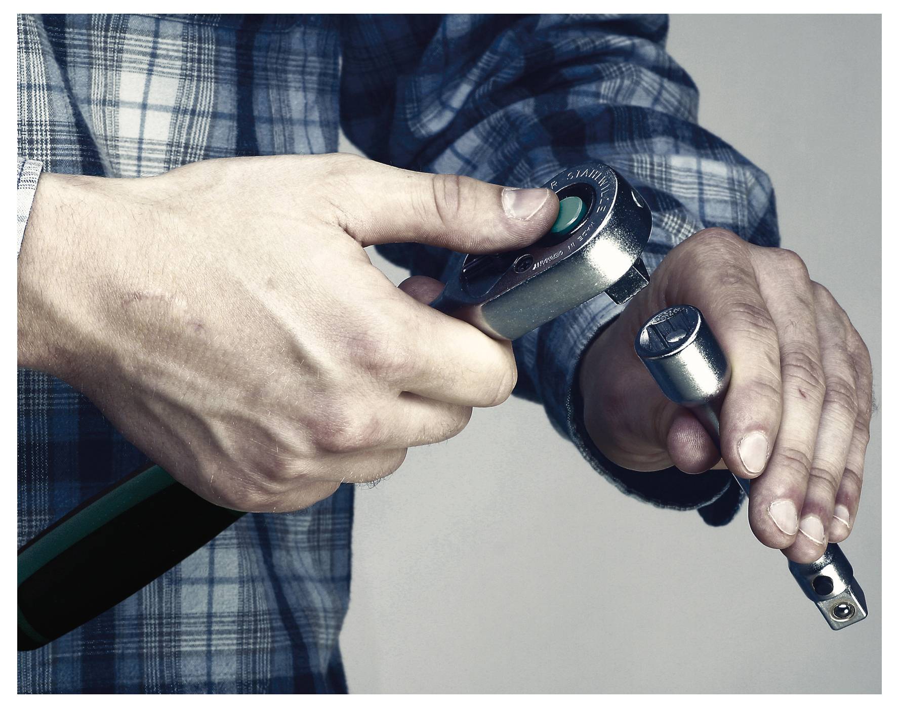Eine Person in einem karierten Hemd befestigt eine Steckdose an einem Ratschenschlüssel und konzentriert sich dabei auf Präzision und mechanische Arbeit.