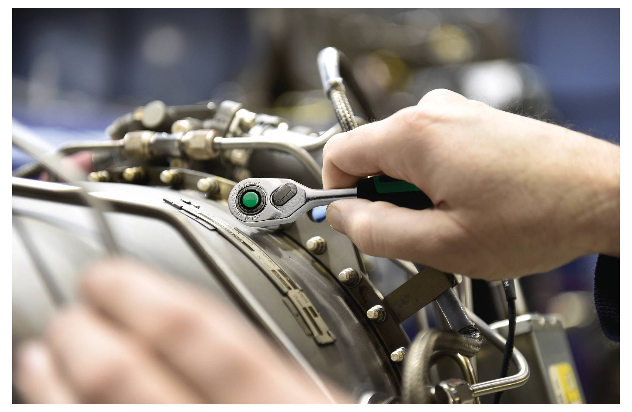 Eine Person nutzt einen Schraubenschlüssel, um Maschinen einzustellen, wobei sie sich auf präzise Ausrichtung konzentriert. Die Umgebung deutet auf ein Industrie- oder Werkstattumfeld hin.